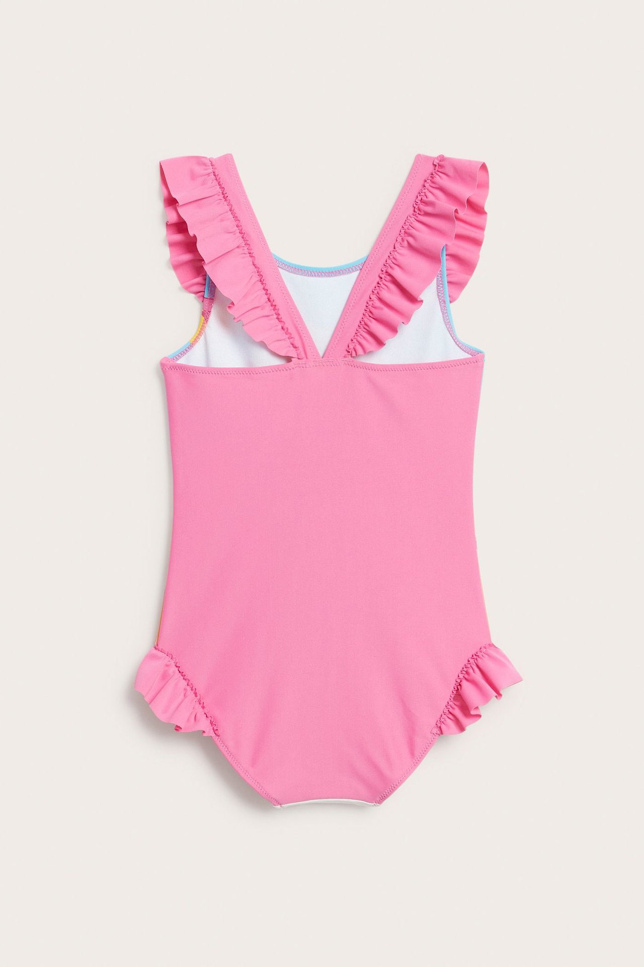 Lasten vaaleanpunainen uimapuku takaa, jossa on röyhelöt olkaimissa ja lahkeissa, ja sininen reunus.