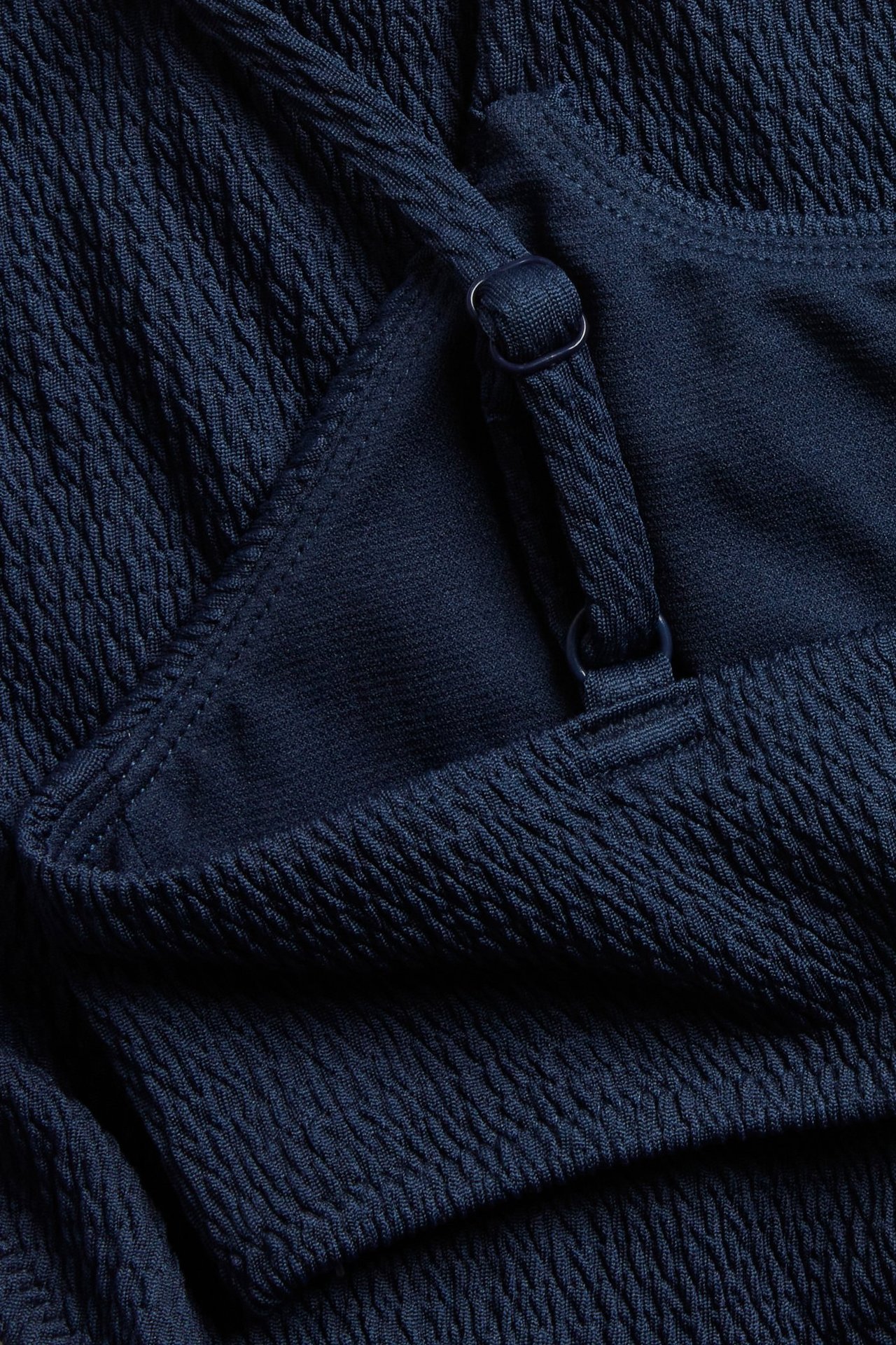 Lähikuva tummansinisestä smokkirintaliivistä, jossa säädettävä olkain ja pieni rengas yksityiskohta.