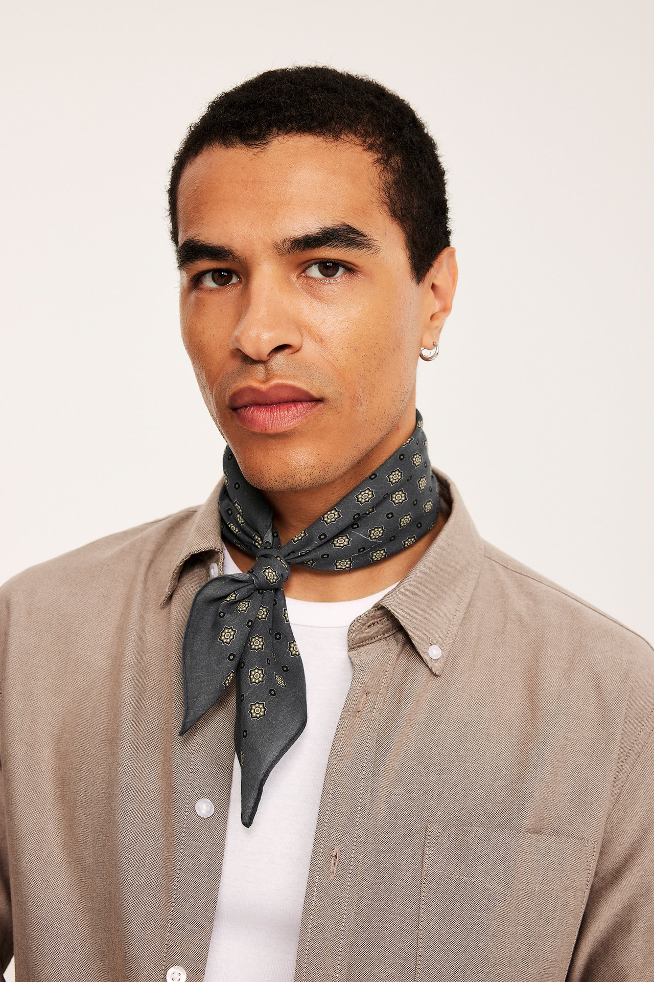 Framifrån en man med en svart mönstrad bomullsscarf och en ljusbrun skjorta.