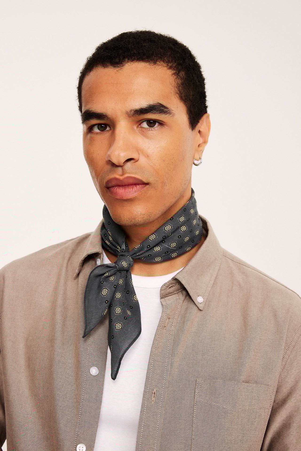 Widok z przodu mężczyzny w czarnym szaliku z bawełny we wzór kwiatowy i jasnobrązowej koszuli.