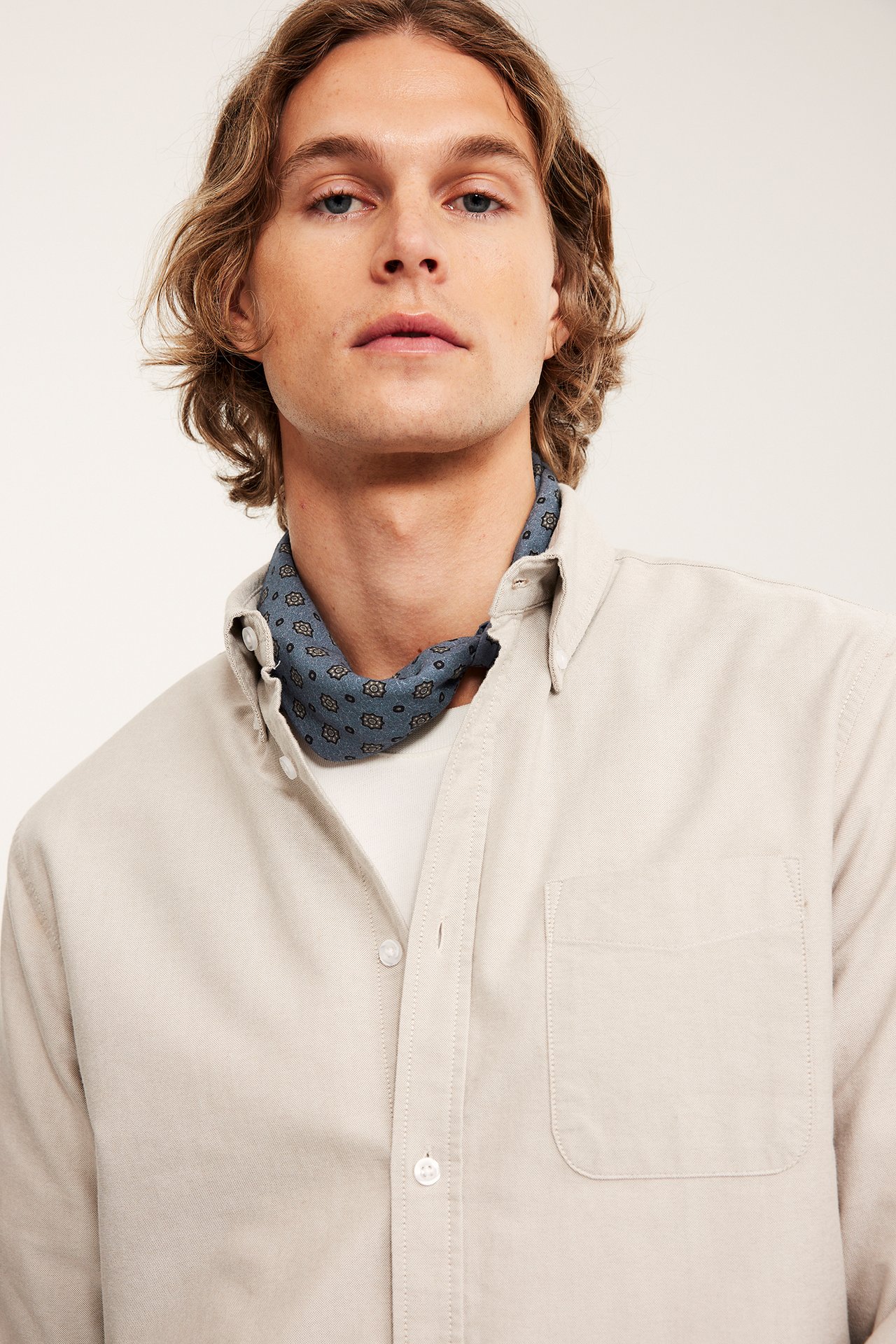 Widok z przodu: mężczyzna w niebieskim bawełnianym szaliku z wzorem na beżowej koszuli i t-shircie.