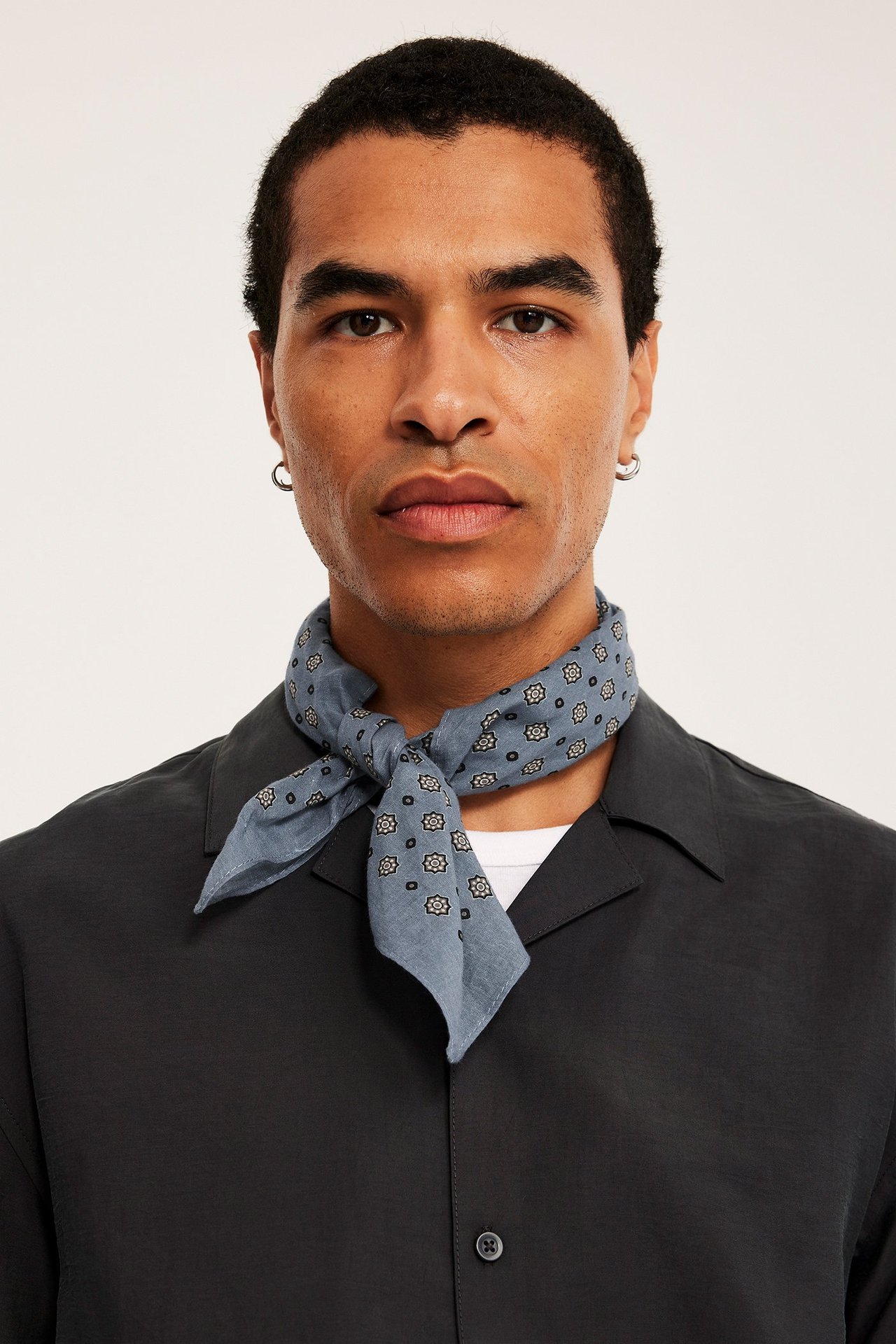 Lähikuva edestä miehestä sinisessä kuviollisessa puuvillahuivissa, tumman paidan ja valkoisen t-paidan päällä.