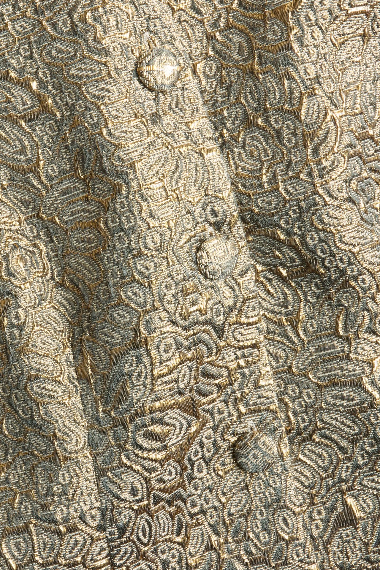Zbliżenie na złoto-szary żakardowy brokatowy materiał sukienki z ozdobnymi guzikami.