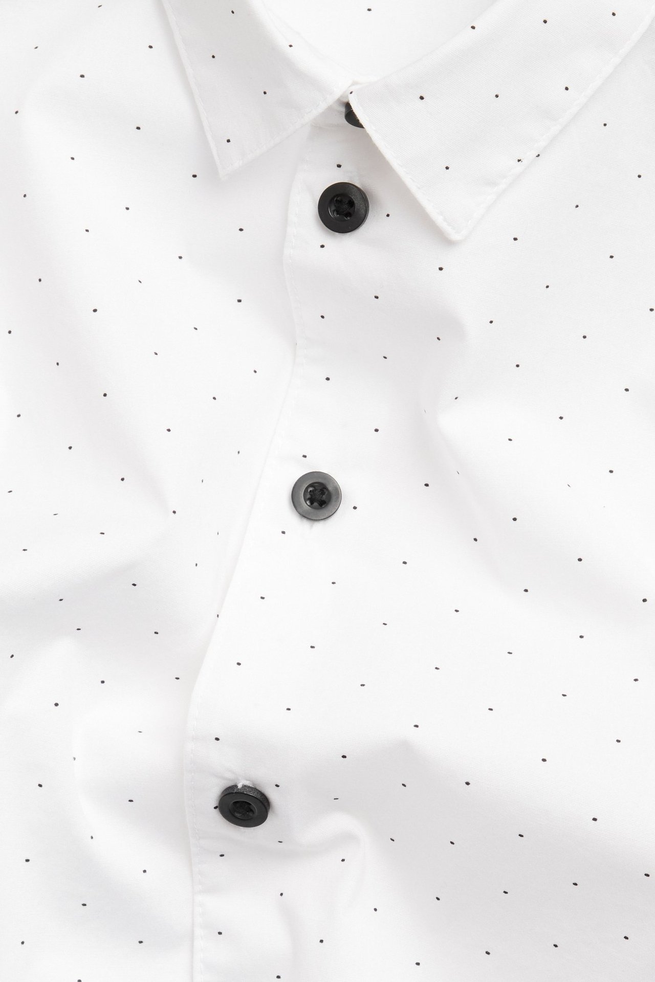 Zbliżenie białej koszuli dziecięcej z bawełny w czarne kropki, z czarnymi guzikami.
