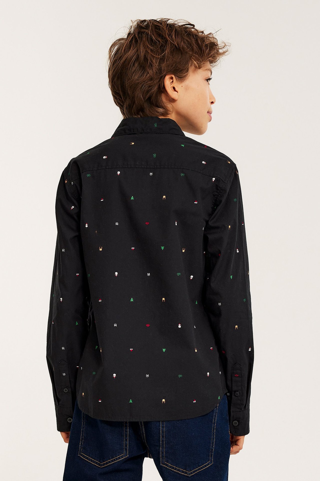 Widok z tyłu: dziecko w czarnej bawełnianej koszuli ze świątecznym wzorem i ciemnych dżinsach.