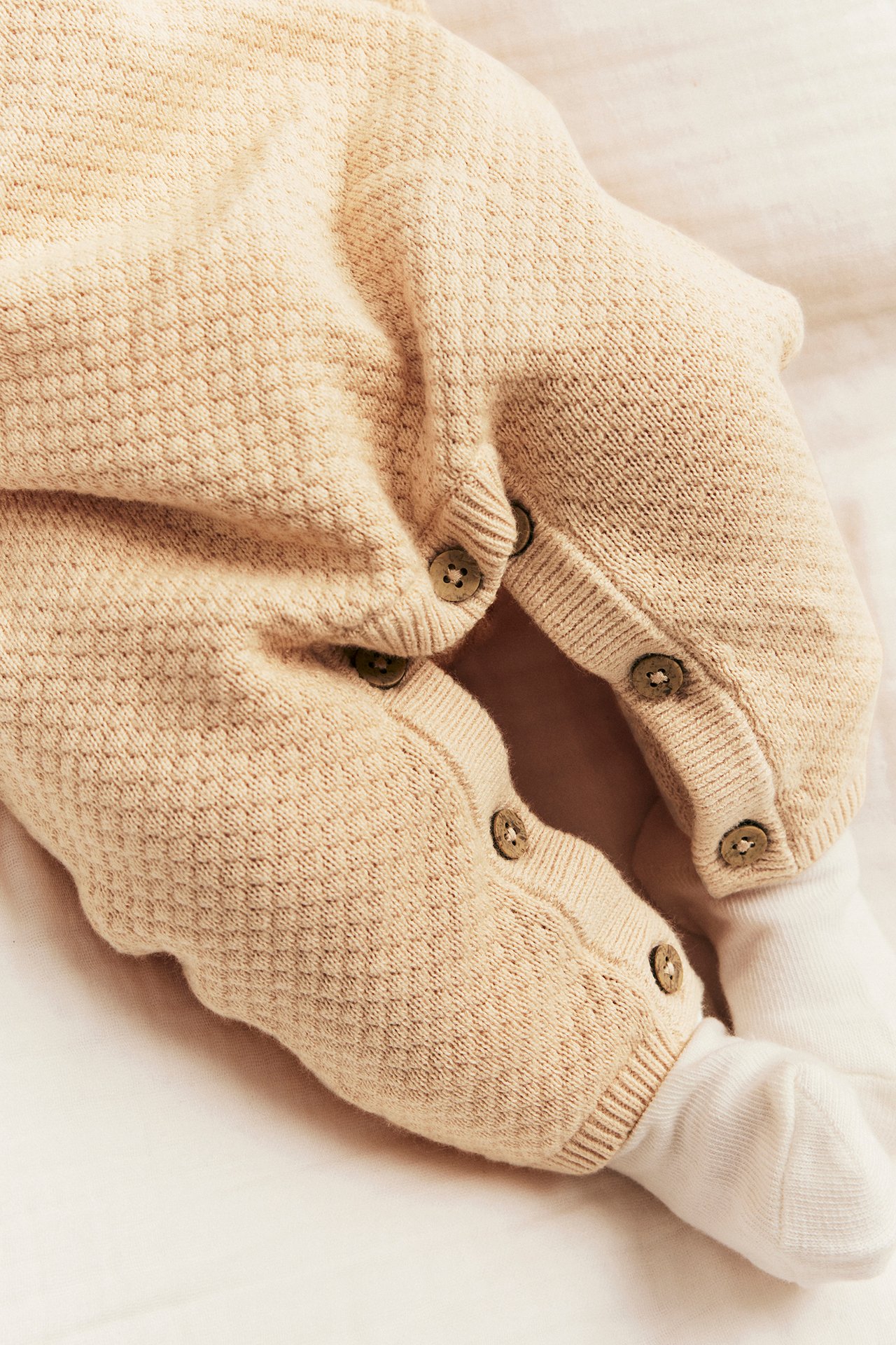 Nærbilde av en baby i en lys oransje strukturstrikket bomullsdress med knapper langs bena, over hvite sokker.