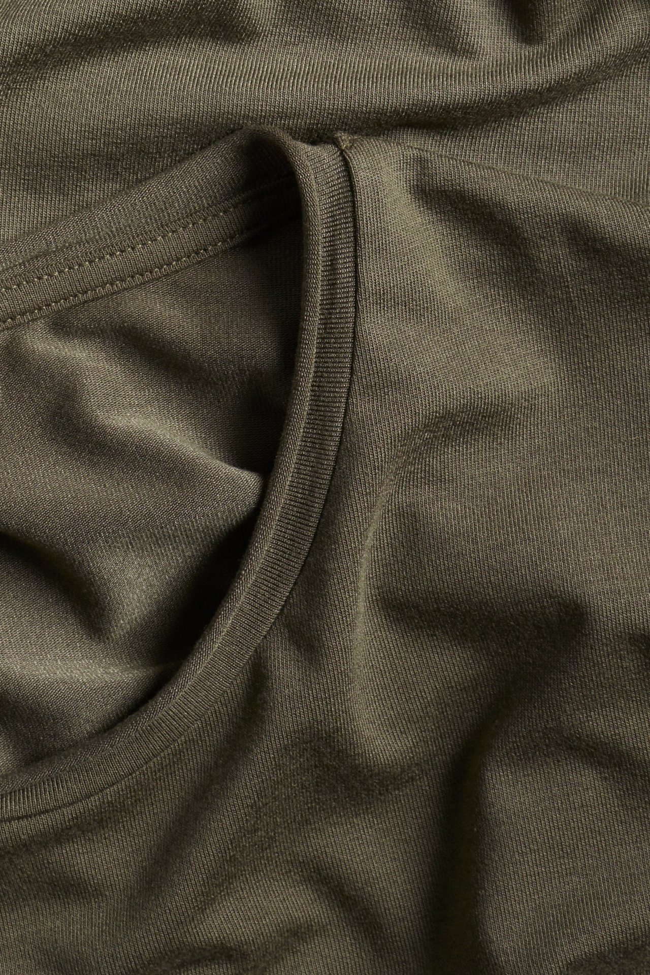 Zbliżenie na khaki zielony top z okrągłym dekoltem z dzianiny, ukazujące teksturę materiału i dekolt.