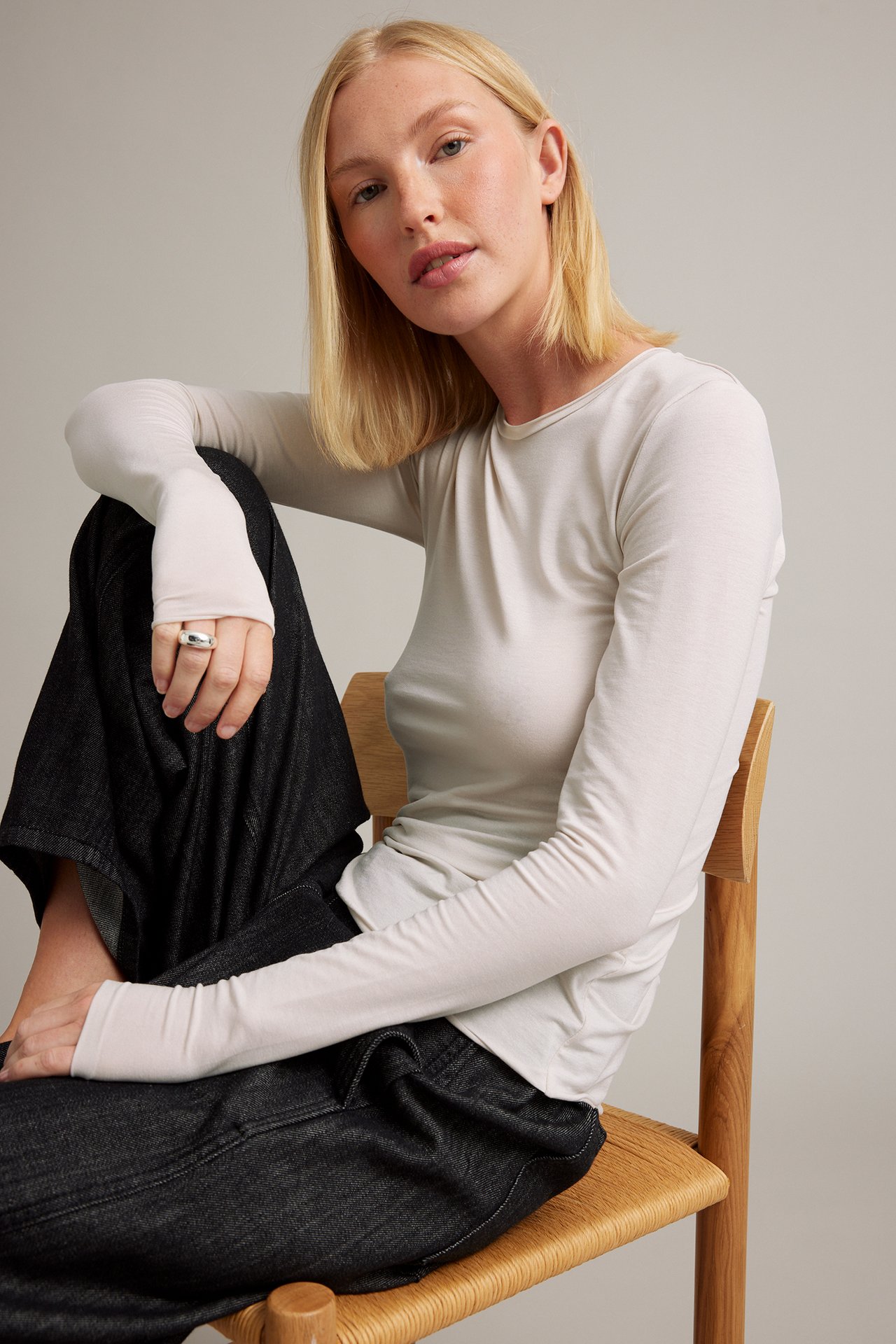 Kvinne iført en lys beige langermet topp, mørkeblå vide jeans og en sølvring.