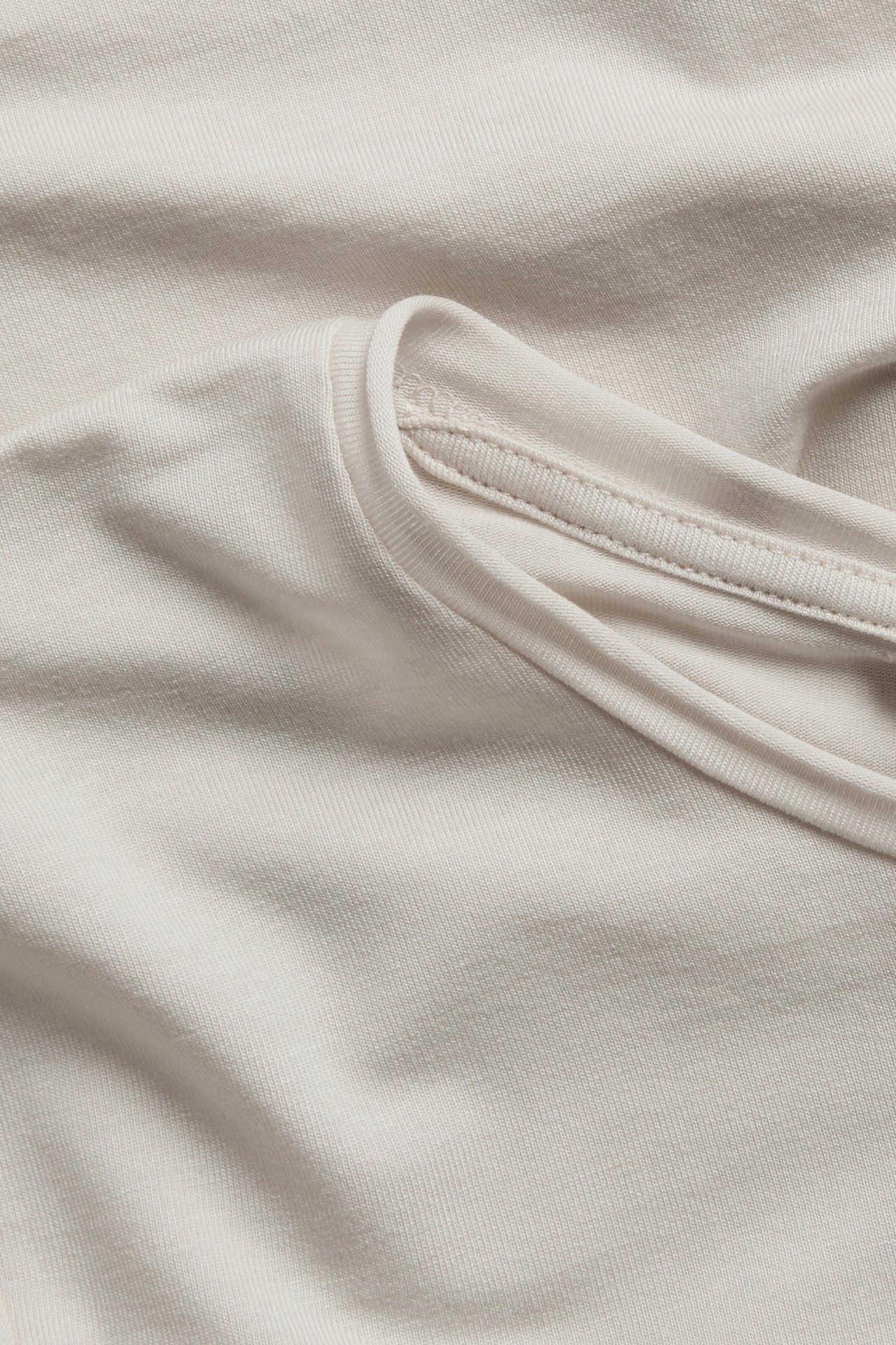Nærbilde av en lys beige jerseyt-skjorte med ribbet hals.