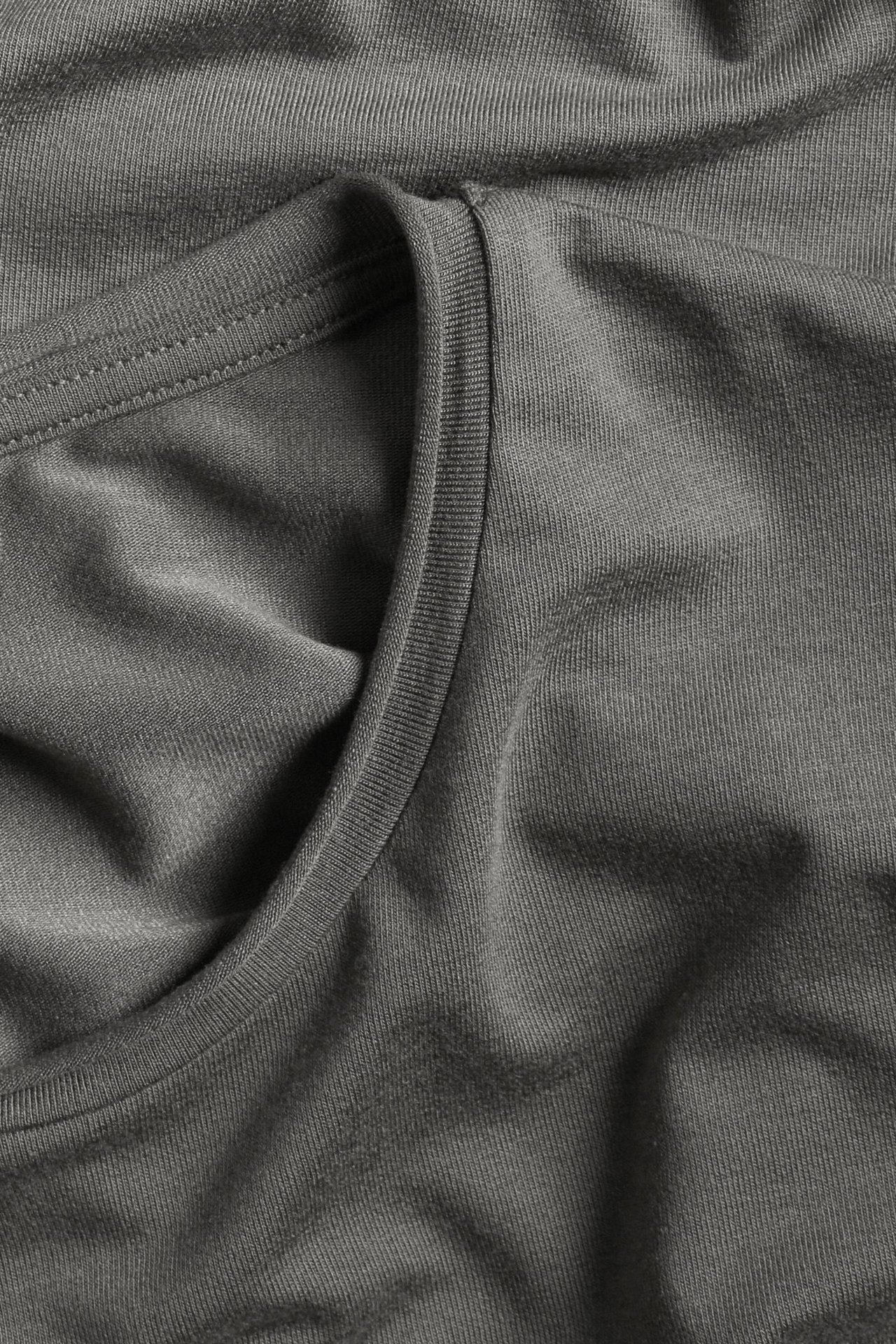 Zbliżenie szarego, jednolitego topu z dżerseju modalowego, z okrągłym dekoltem i subtelnymi prążkami.