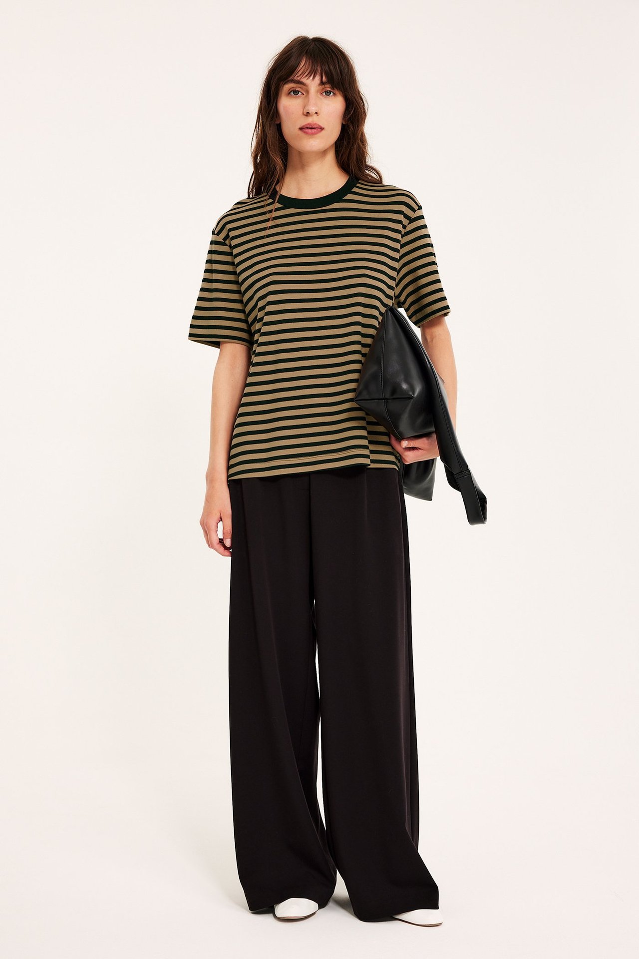 Frontutsikt: Kvinne har på oversized beige og svartstripet t-skjorte, svarte vide bukser, hvite sko, holder svart veske.