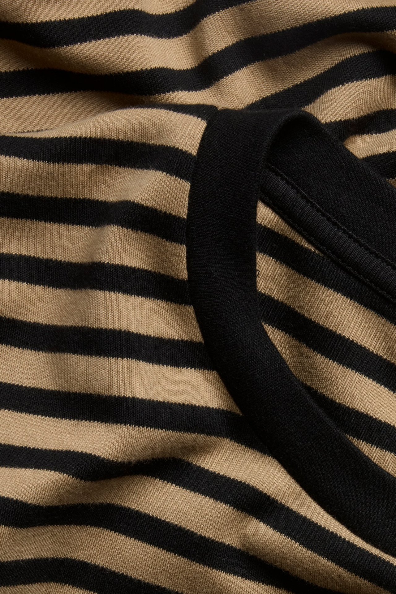 Zbliżenie beżowo-czarnego, pasiasto-oversize'owego bawełnianego T-shirtu z czarnym prążkowanym dekoltem.
