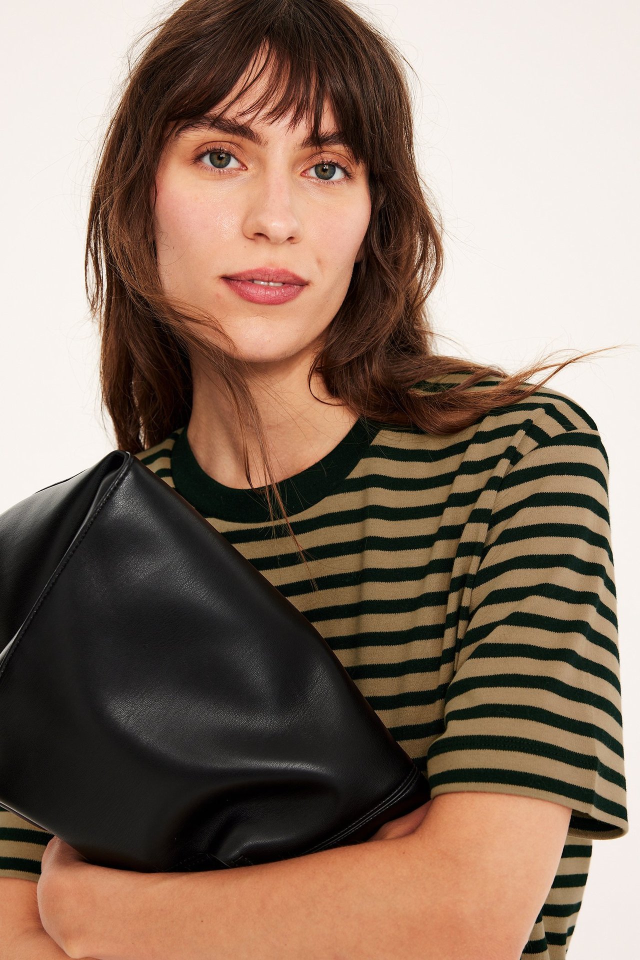 Nærbilde av kvinne i oversized beige og mørkegrønn stripete bomulls-T-skjorte, holder en svart håndveske.