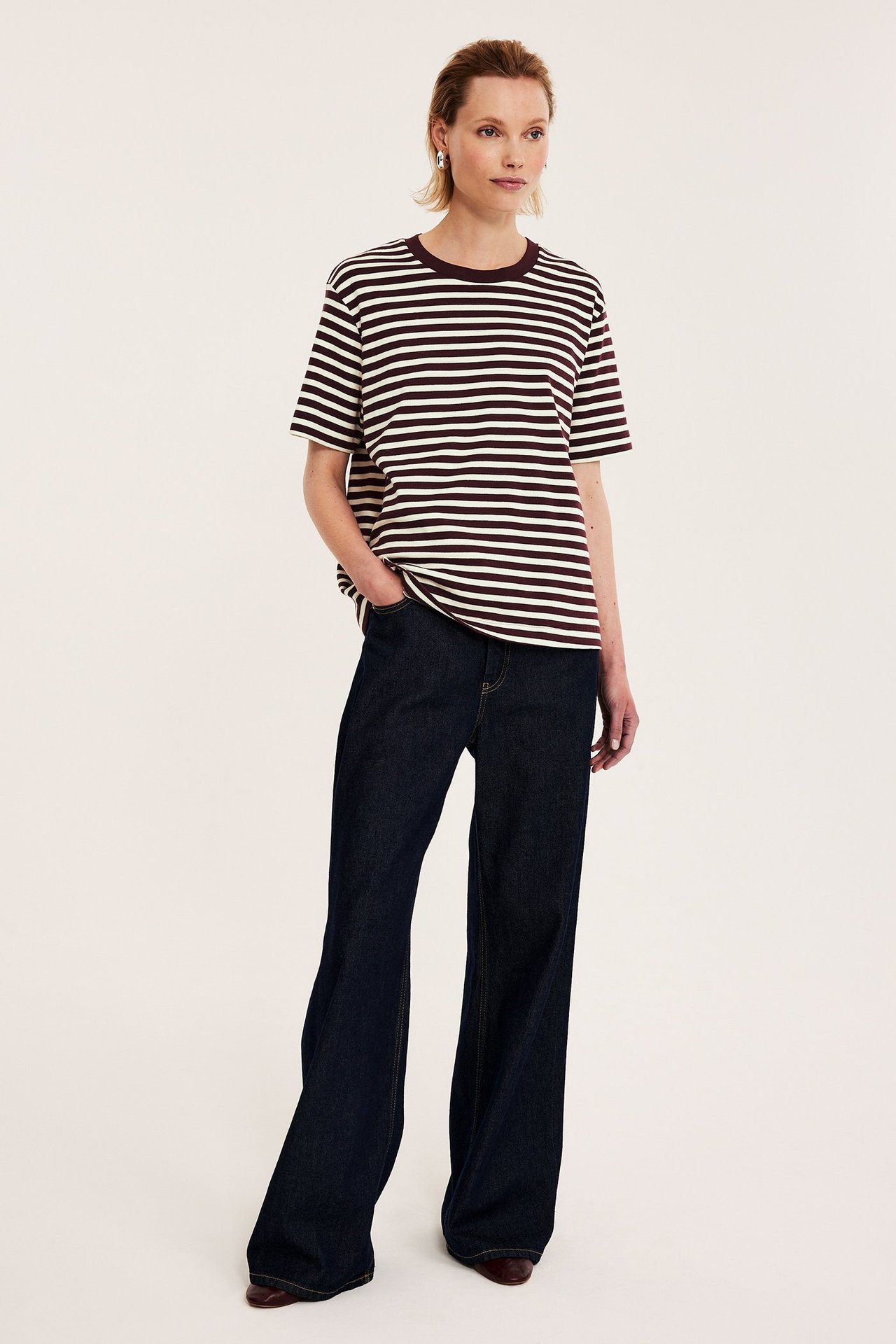 Frontbilde av kvinne i offwhite og mørkstripet oversized bomulls-t-skjorte og mørkeblå vide jeans.