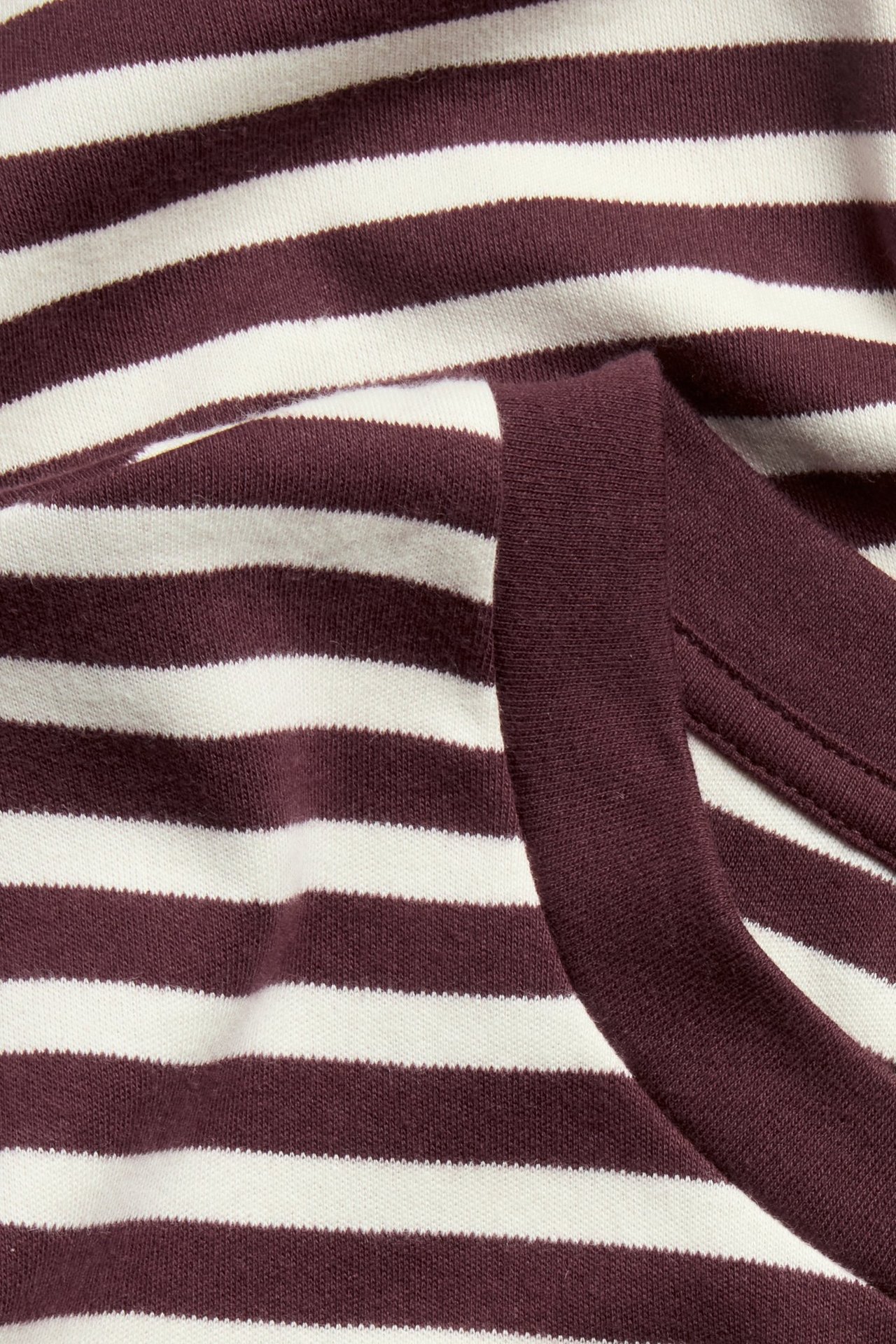 Zbliżenie na biało-bordową, pasiastą, bawełnianą koszulkę oversize z prążkowanym dekoltem.