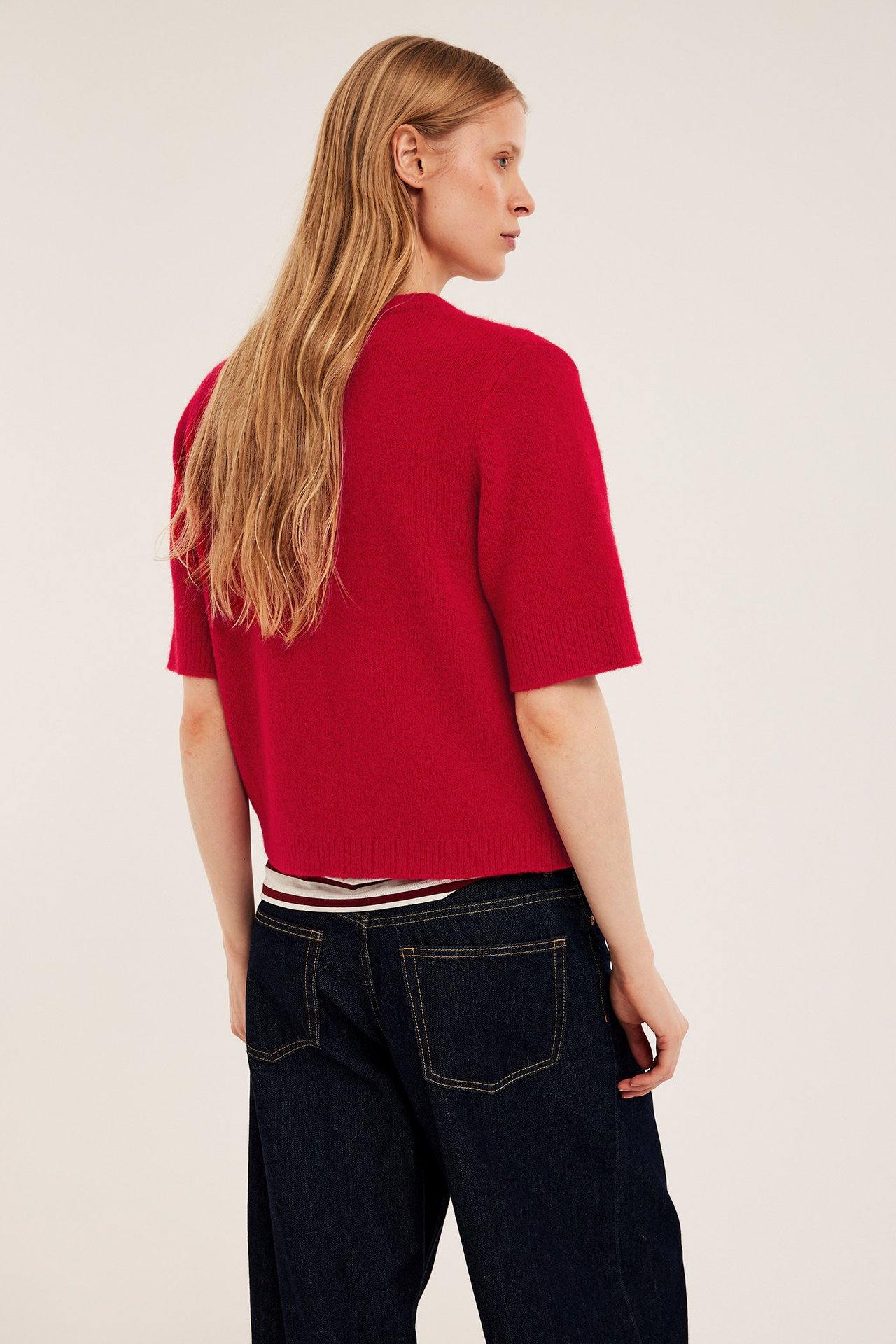 Ryggvy av kvinna i röd kortärmad stickad pullover över randig topp och mörkblå jeans.
