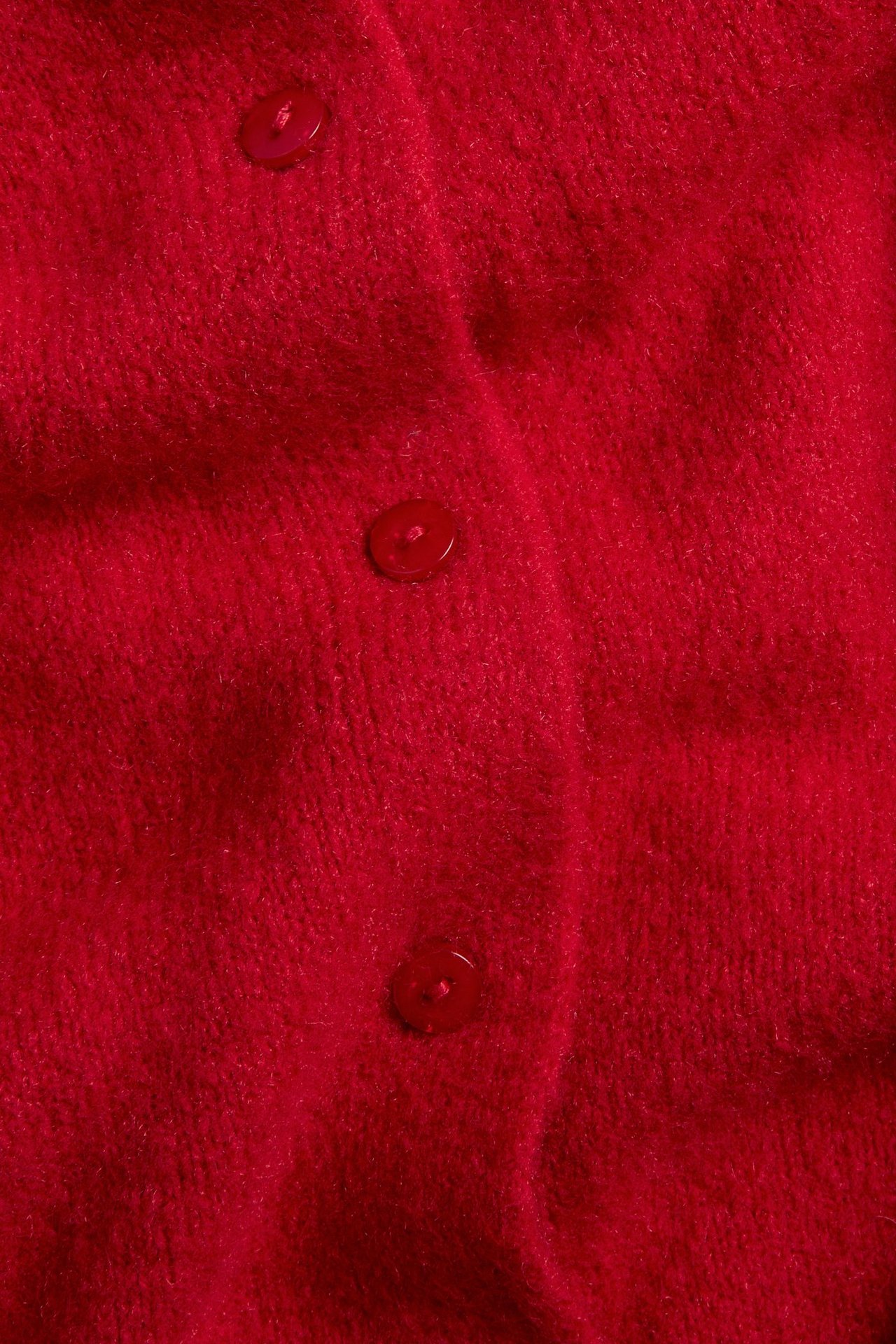 Zbliżenie czerwonego dzianinowego kardiganu z trzema guzikami na miękkim materiale.