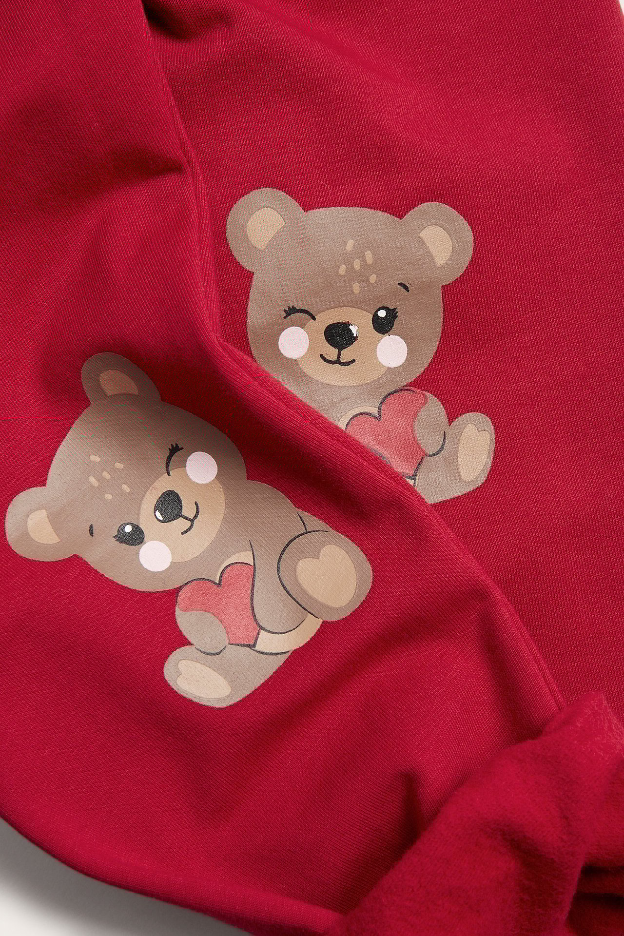 Zbliżenie czerwonych legginsów dziecięcych z dwoma aplikacjami brązowych misiów, każdy trzymający czerwone serce.