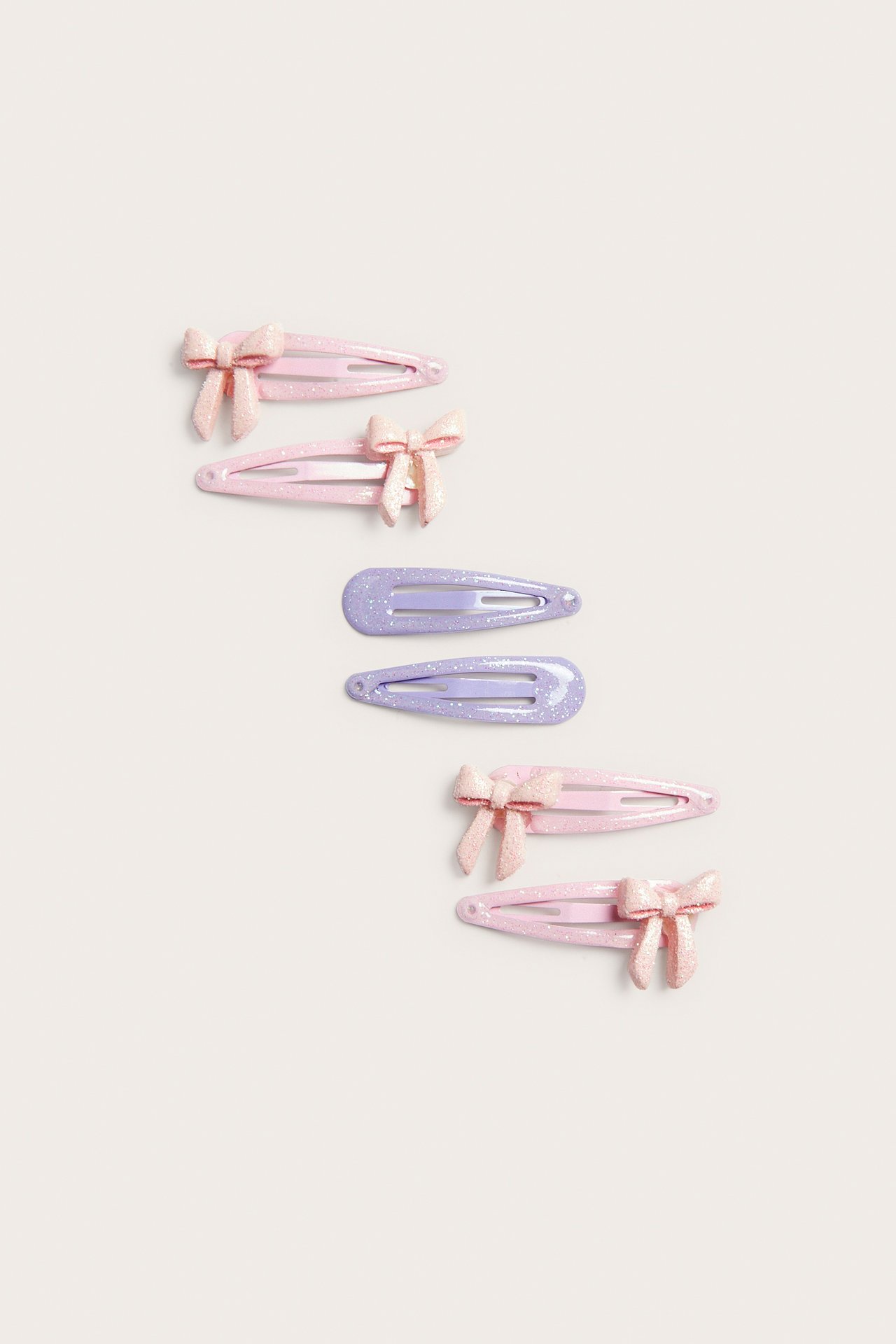 Ovanifrån: sex glittriga hårspännen i plast; fyra ljusrosa med rosetter, två ljuslila.