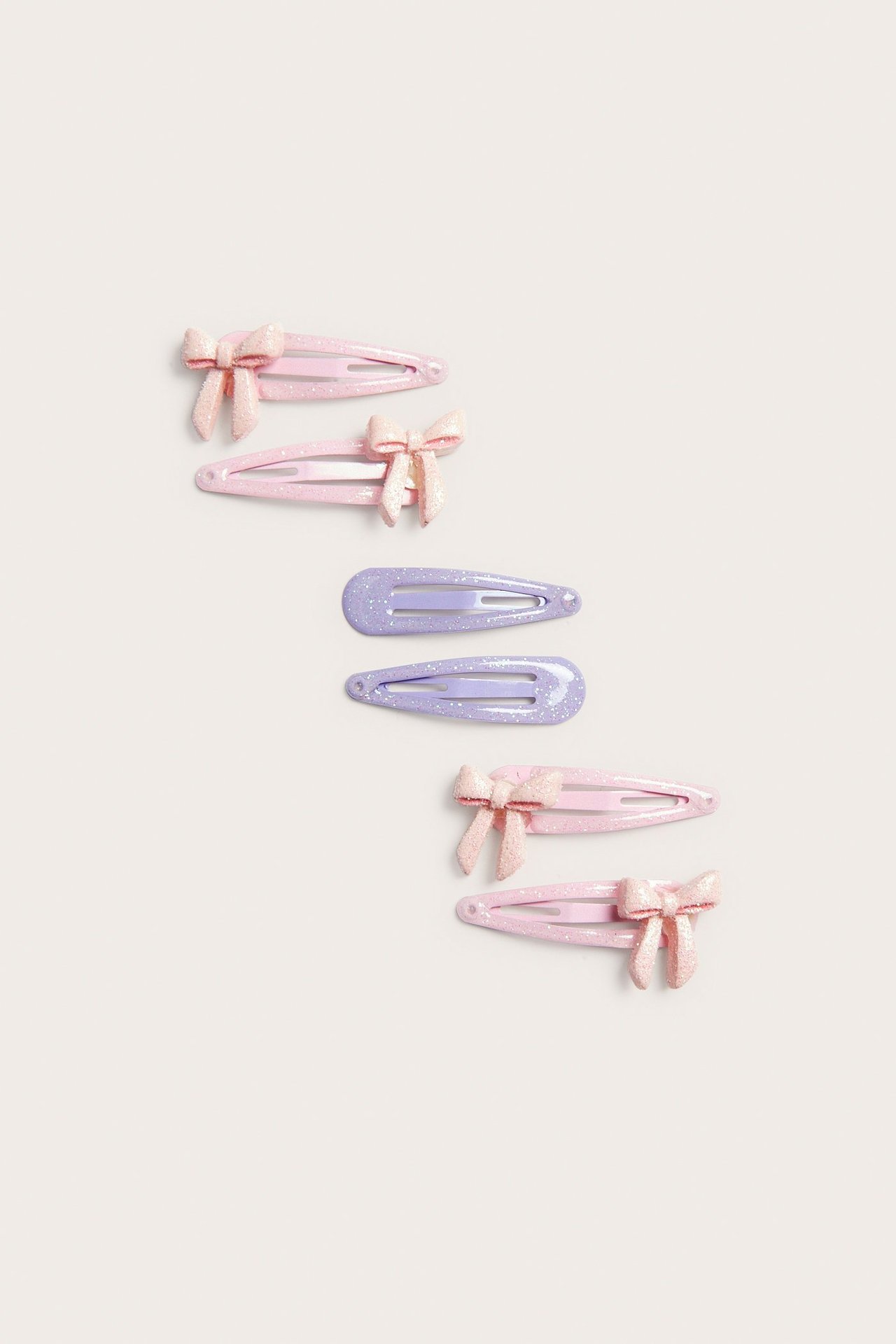 Widok z góry: sześć brokatowych, plastikowych spinek; cztery jasnoróżowe z kokardami, dwie jasnofioletowe.