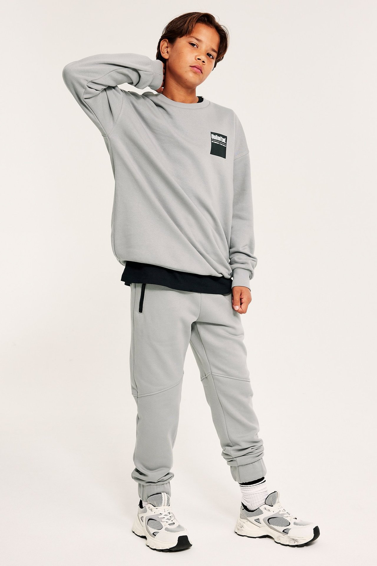 Młody chłopak w szarych joggerach i sweatshirt, stojący na wprost.