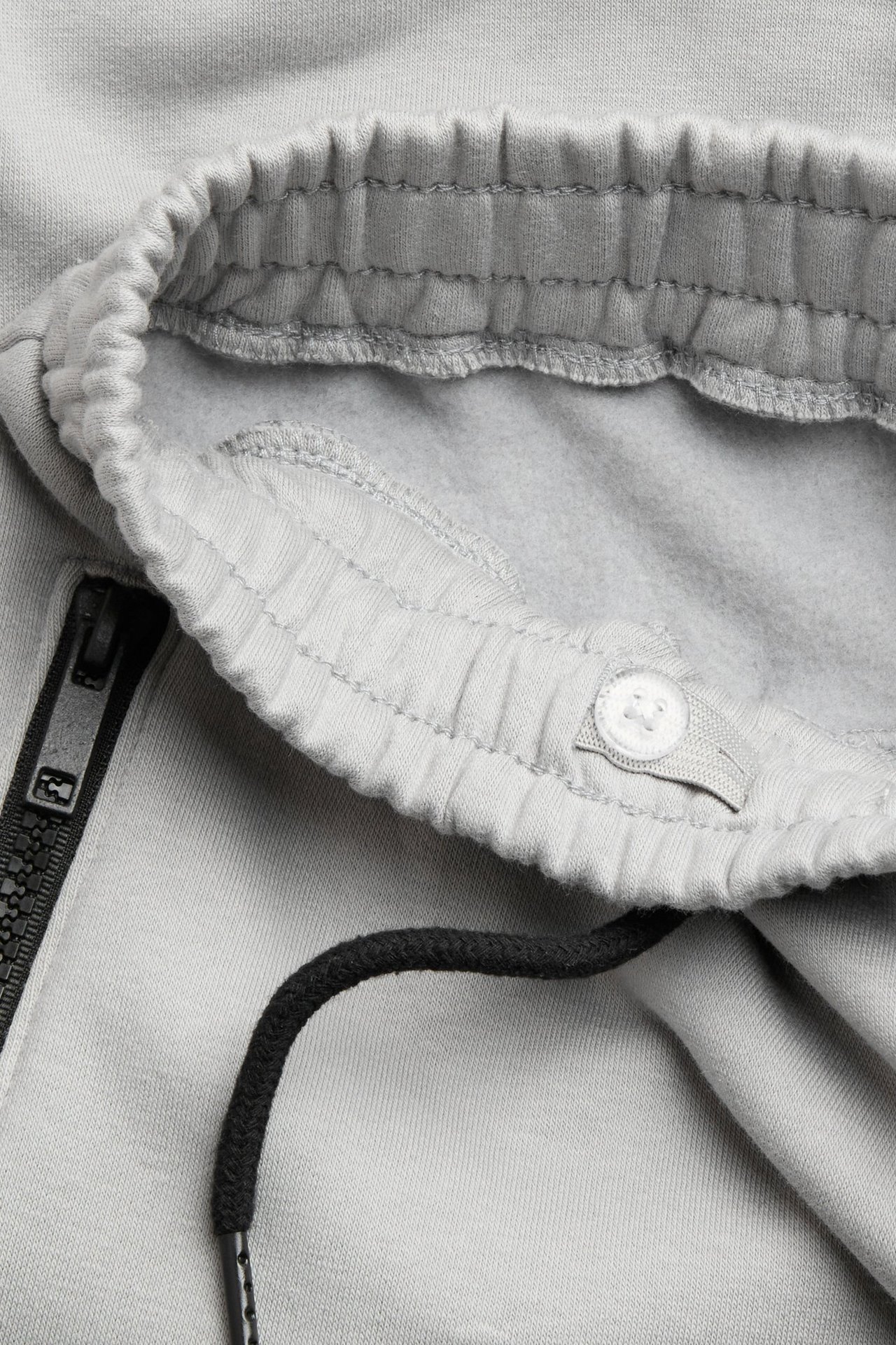 Zbliżenie szarych bawełnianych spodni dresowych z elastycznym pasem, czarnym sznurkiem i kieszenią na zamek.