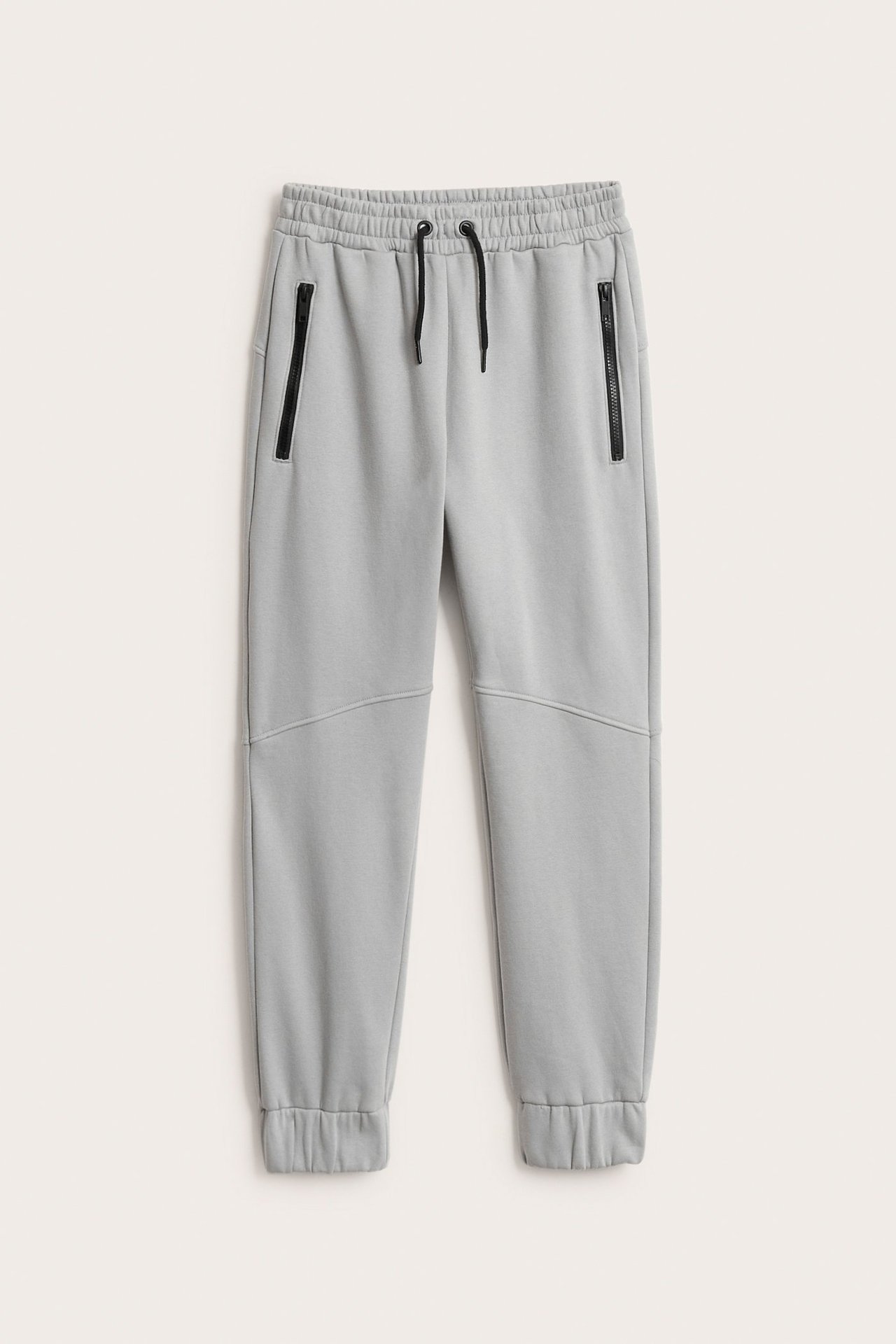 Widok z przodu: Szare dresy z bawełny z elastycznym pasem, czarnym sznurkiem, kieszeniami na zamek i panelami.