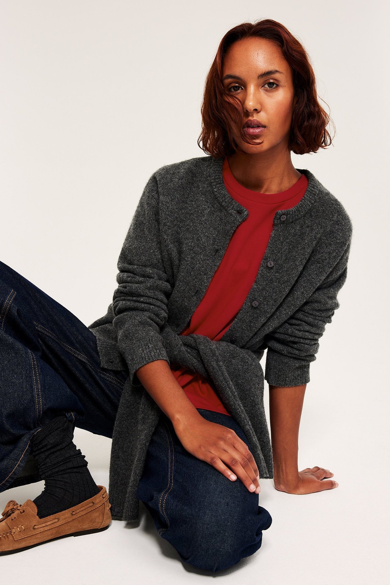 Kvinne i rød oversized T-skjorte, grå cardigan, sittende, front view.