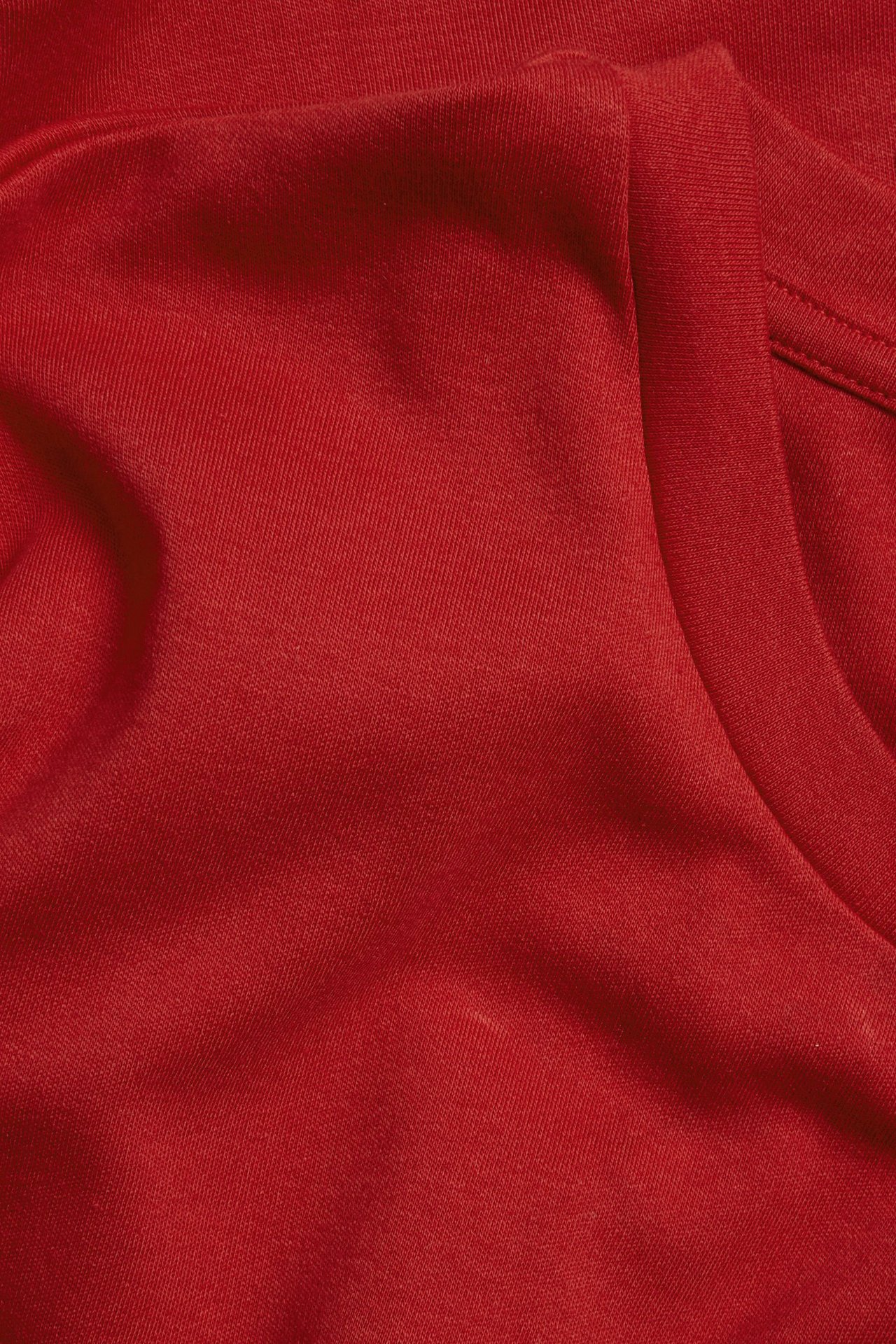 Zbliżenie czerwonej, obszernej koszulki z bawełny interlock, ukazujące fakturę materiału i część dekoltu.