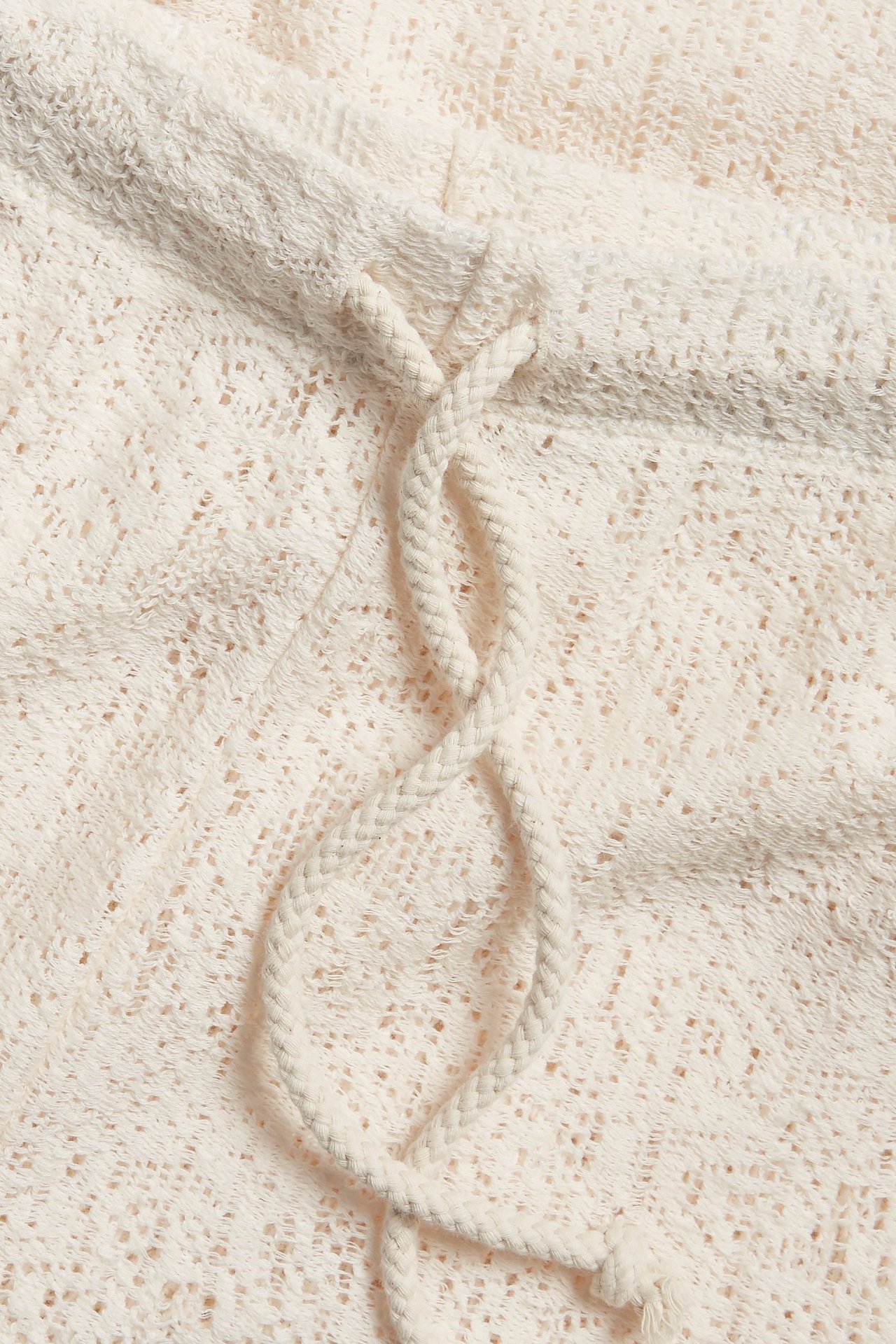 Zbliżenie na ecru szerokie koronkowe spodnie z plecionym sznurkiem w pasie.