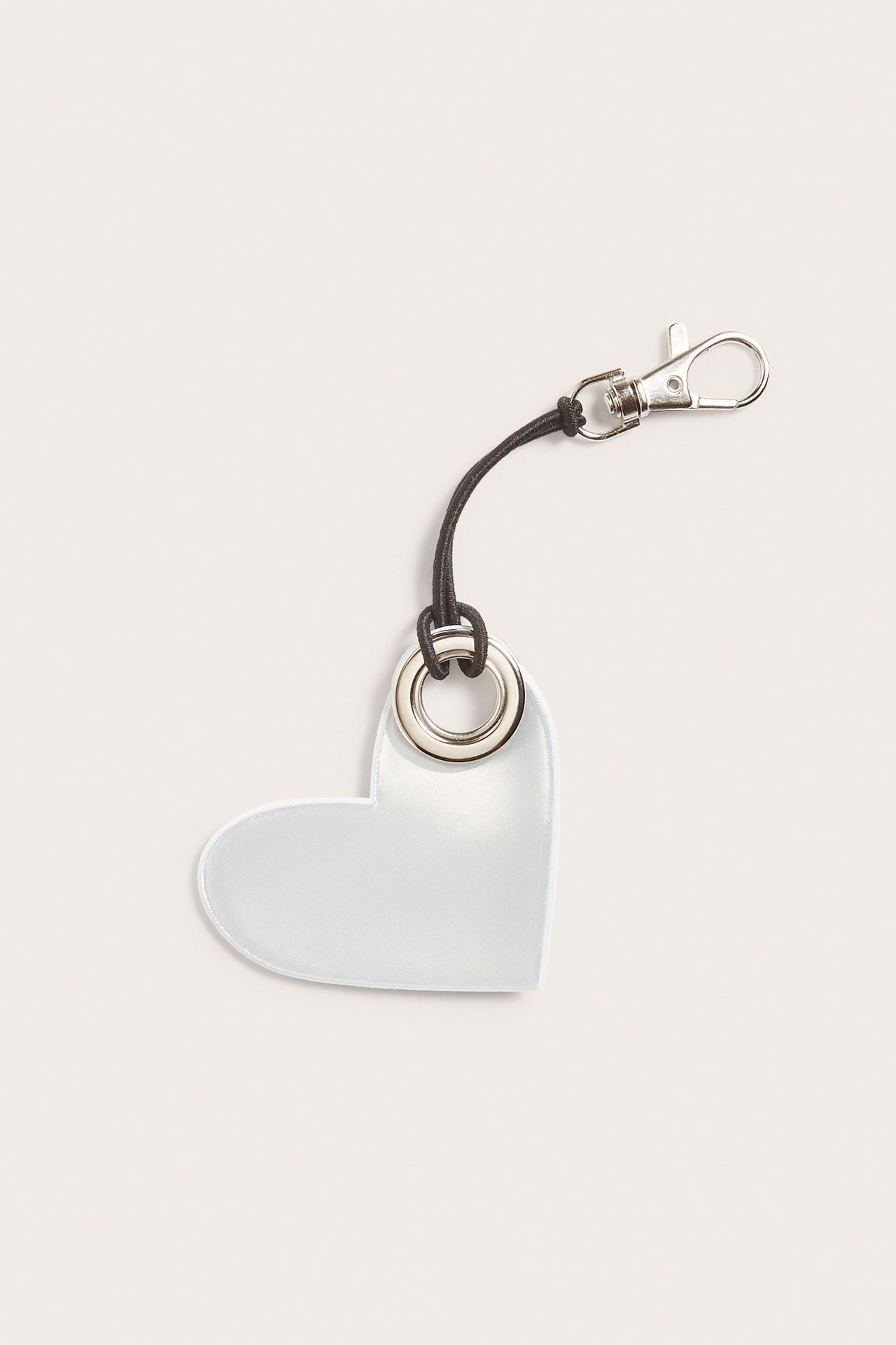 Zbliżenie srebrnego, sercowatego odblasku z tworzywa sztucznego z czarnym sznurkiem i metalowym karabińczykiem.