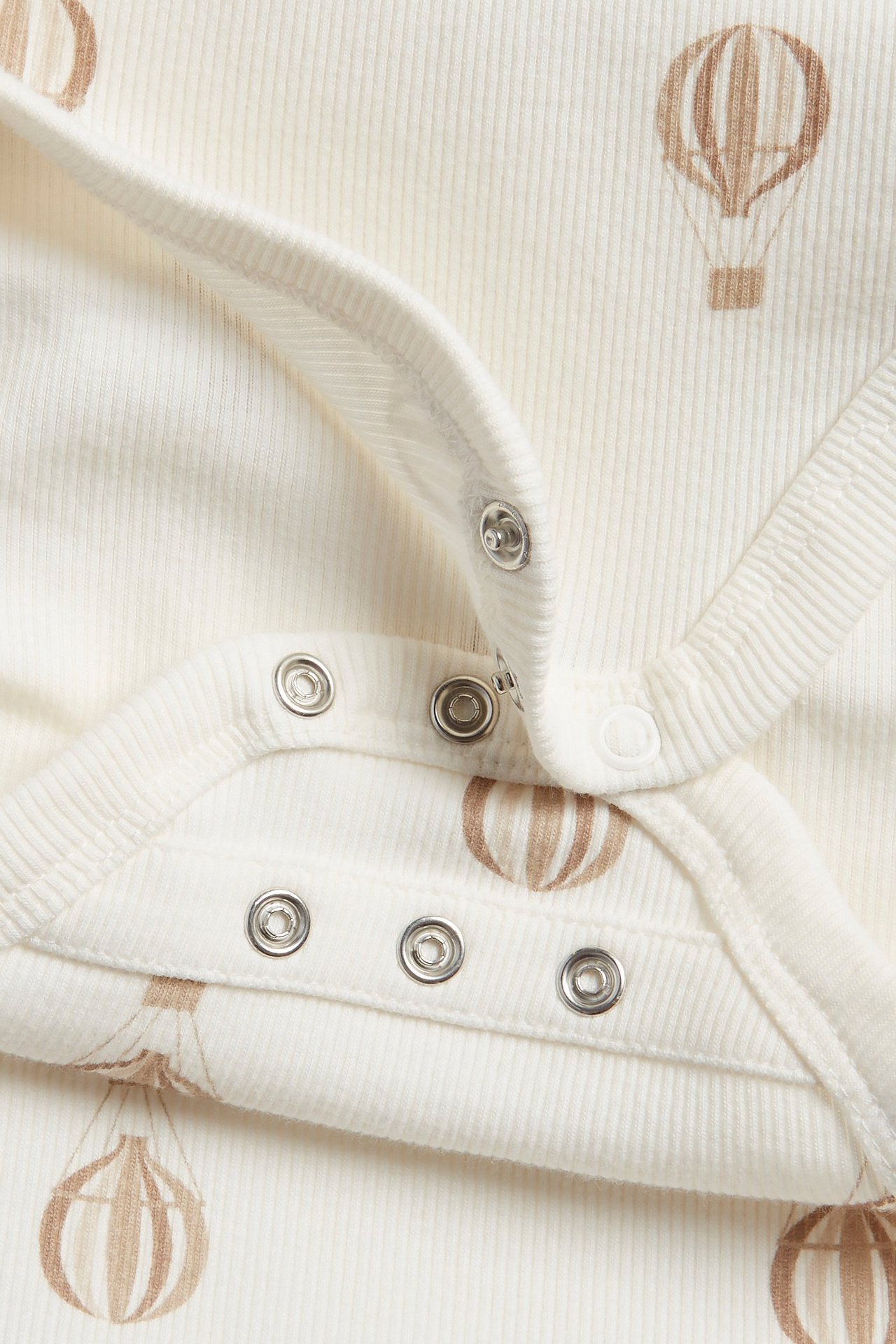 Närbild på en beige ribbad babybody med brunt luftballongsmönster och tryckknappar.