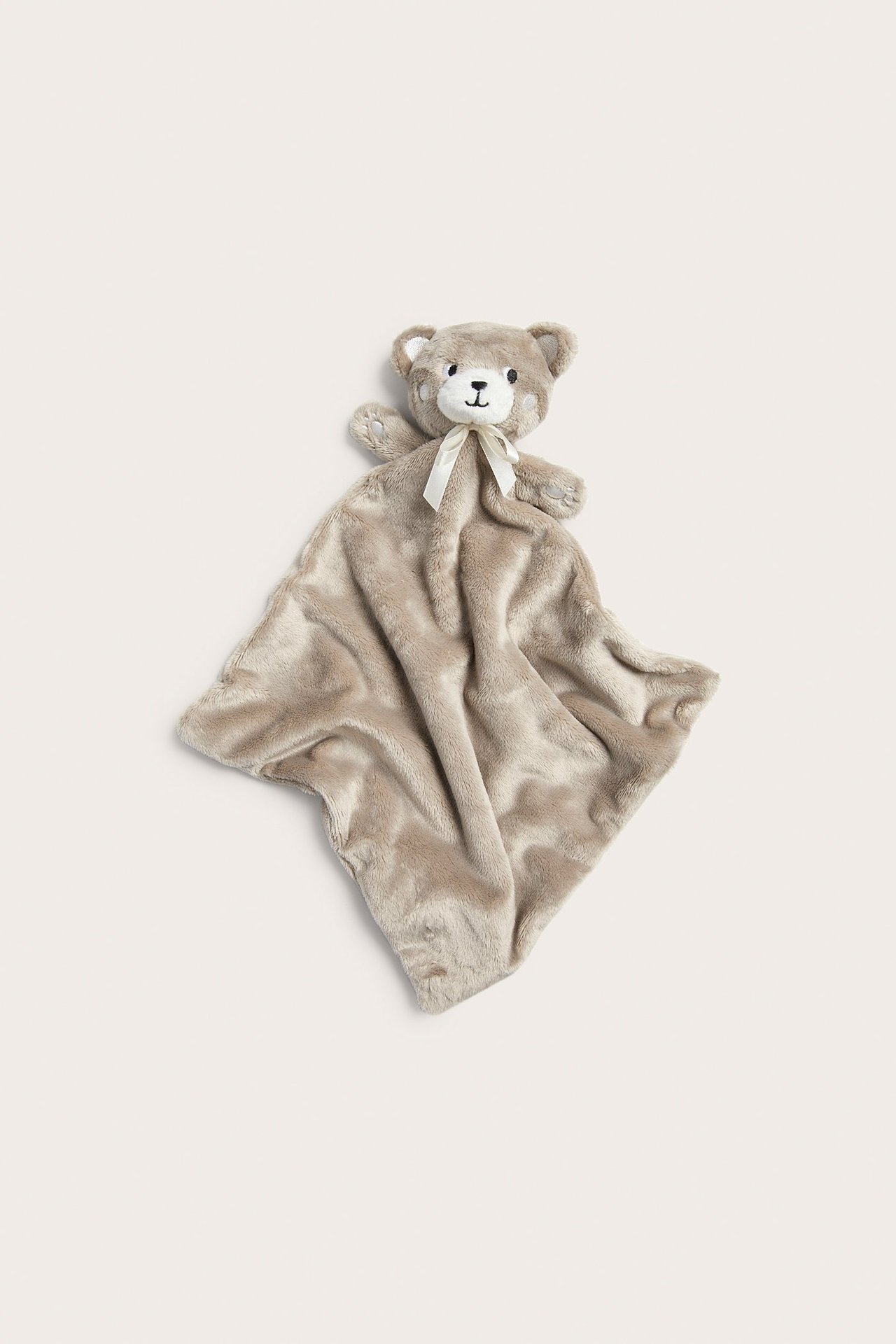 Ylhäältä kuvattu pehmeä, beige pehmolelunuttu huopa, jossa nallekarhun pää ja vaalea rusetti.