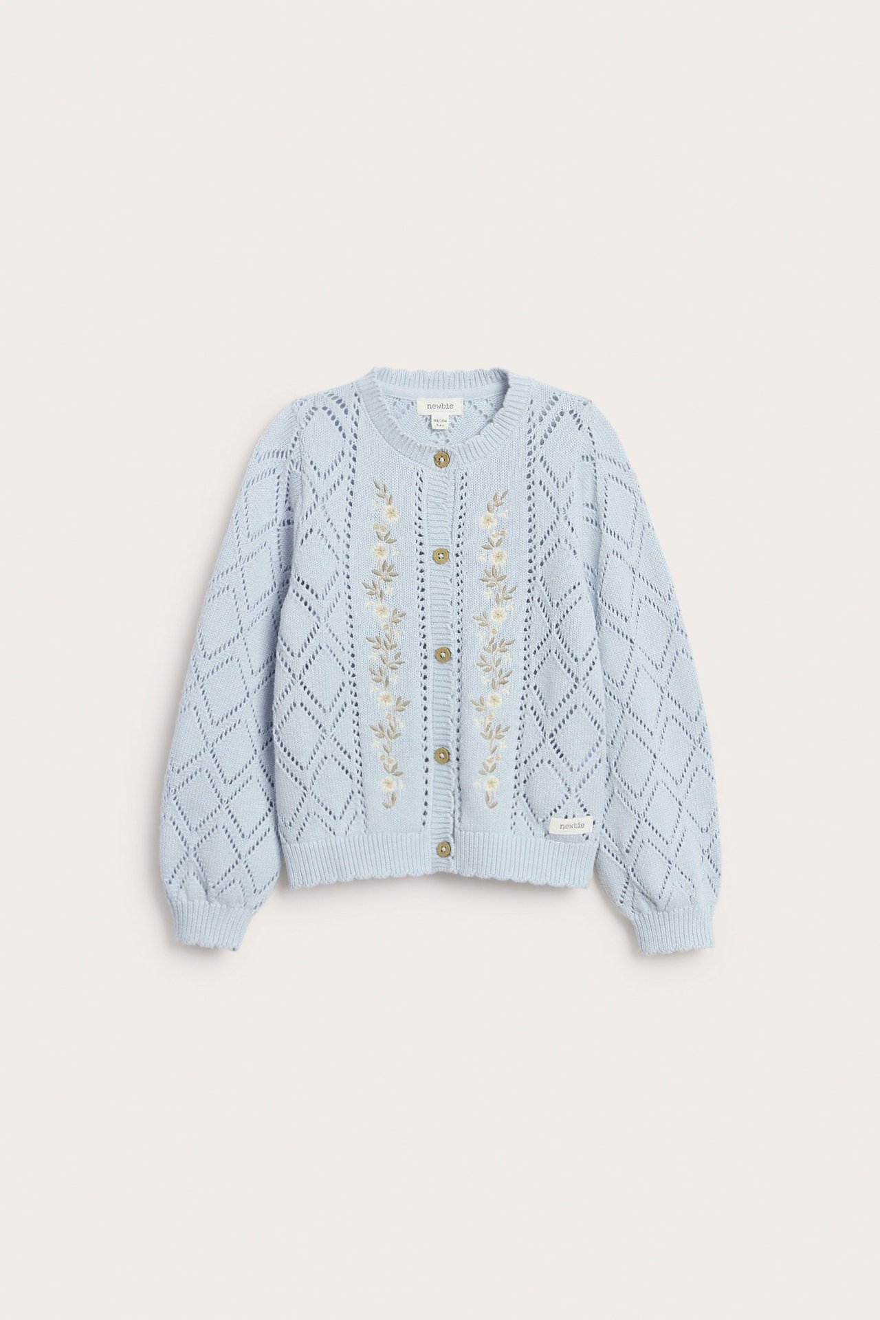 Edestä näkymä vaaleansinisestä kuviollisesta lasten neulepaidasta, jossa kirjaillut kukat ja Newbie-napit.