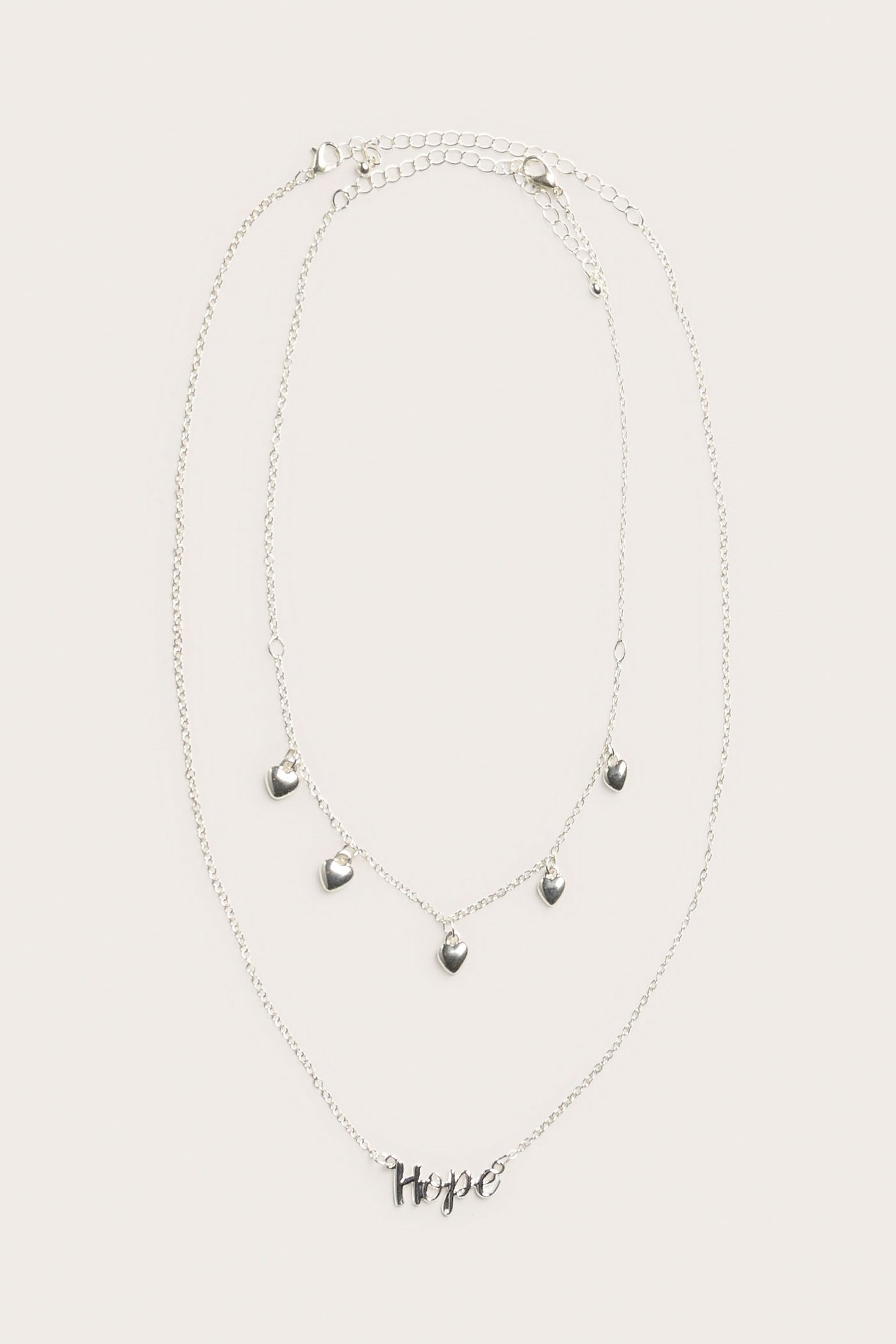 Övervy av två silverhalsband, ett med texten 'Hope', ett med små hjärtformade berlocker.