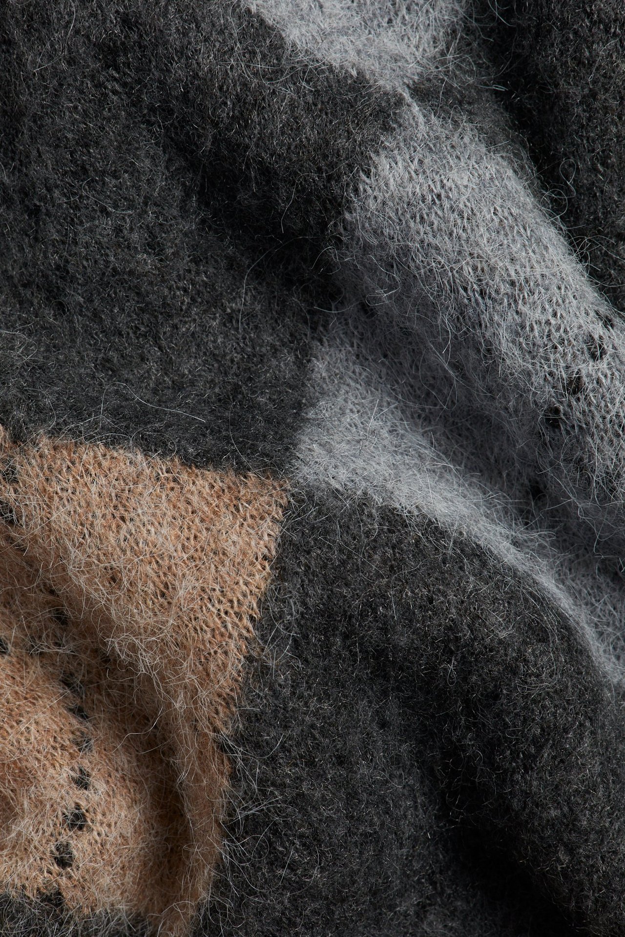 Nærbilde av en myk argyle-strikkegenser i mørkegrått, lysegrått og beige.