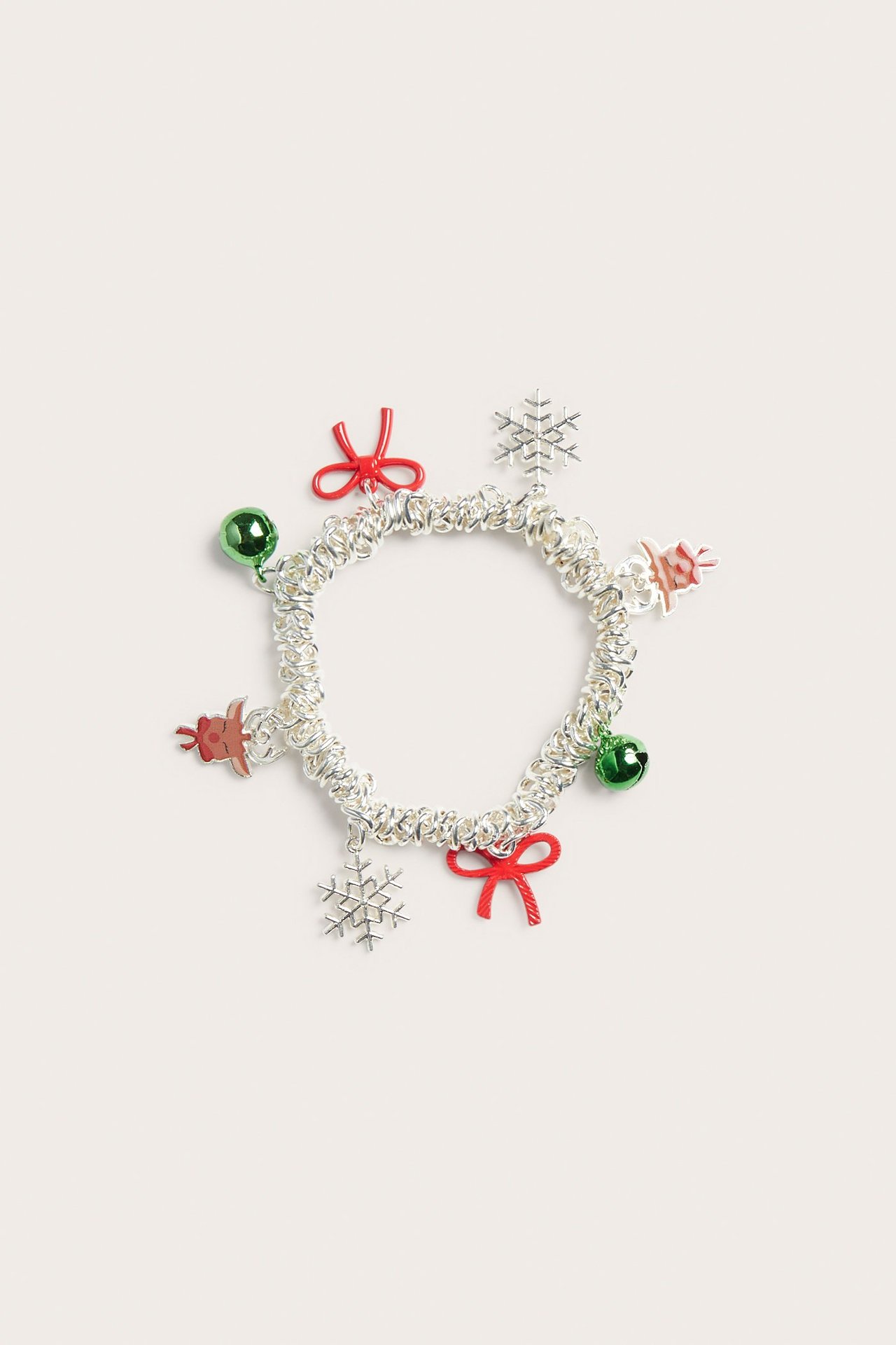Lähikuva hopeisesta metallirannekorusta, jossa joulukoristeita: punaisia rusetteja, lumihiutaleita, vihreitä kelloja, pieniä poroja.