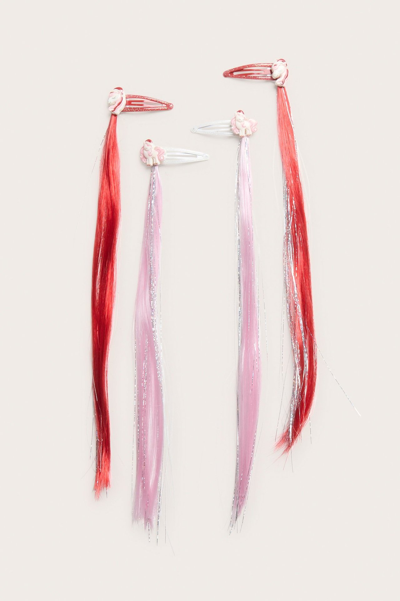 Widok z góry: cztery dziecięce spinki z doczepianymi włosami. Dwie czerwone, dwie różowe z brokatem, z jednorożcami.