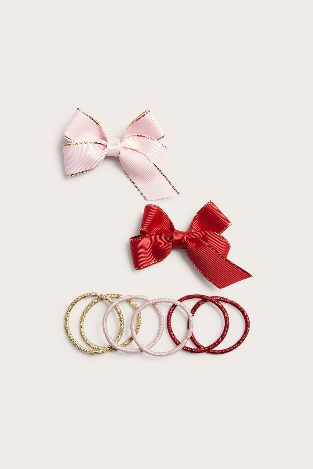 Närbild av ett håraccessoarpaket: rosa och röda rosettklämmor, med guld-, rosa- och röda glittersnoddar.