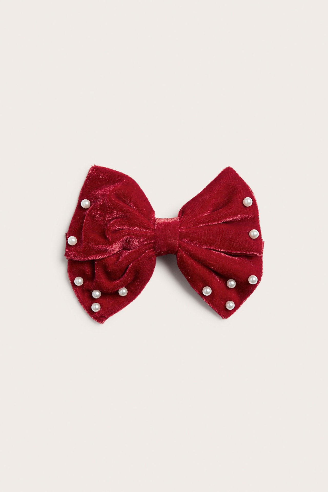 Framsida av röd sammetshårklämma med rosett och vita pärlor.