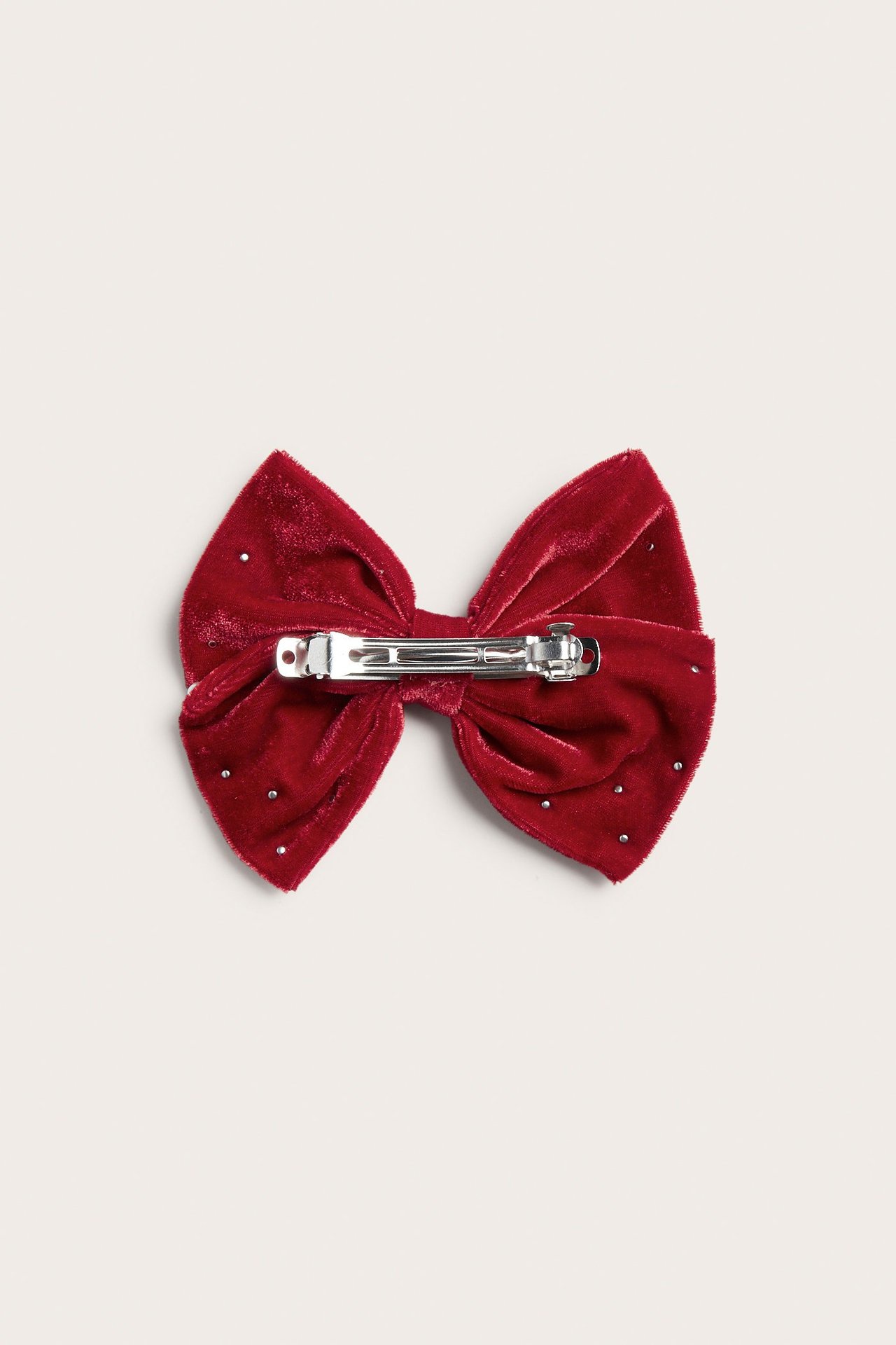 Bakifrån: röd sammetsrosett hårklämma med silvernitar och en metallklämma.