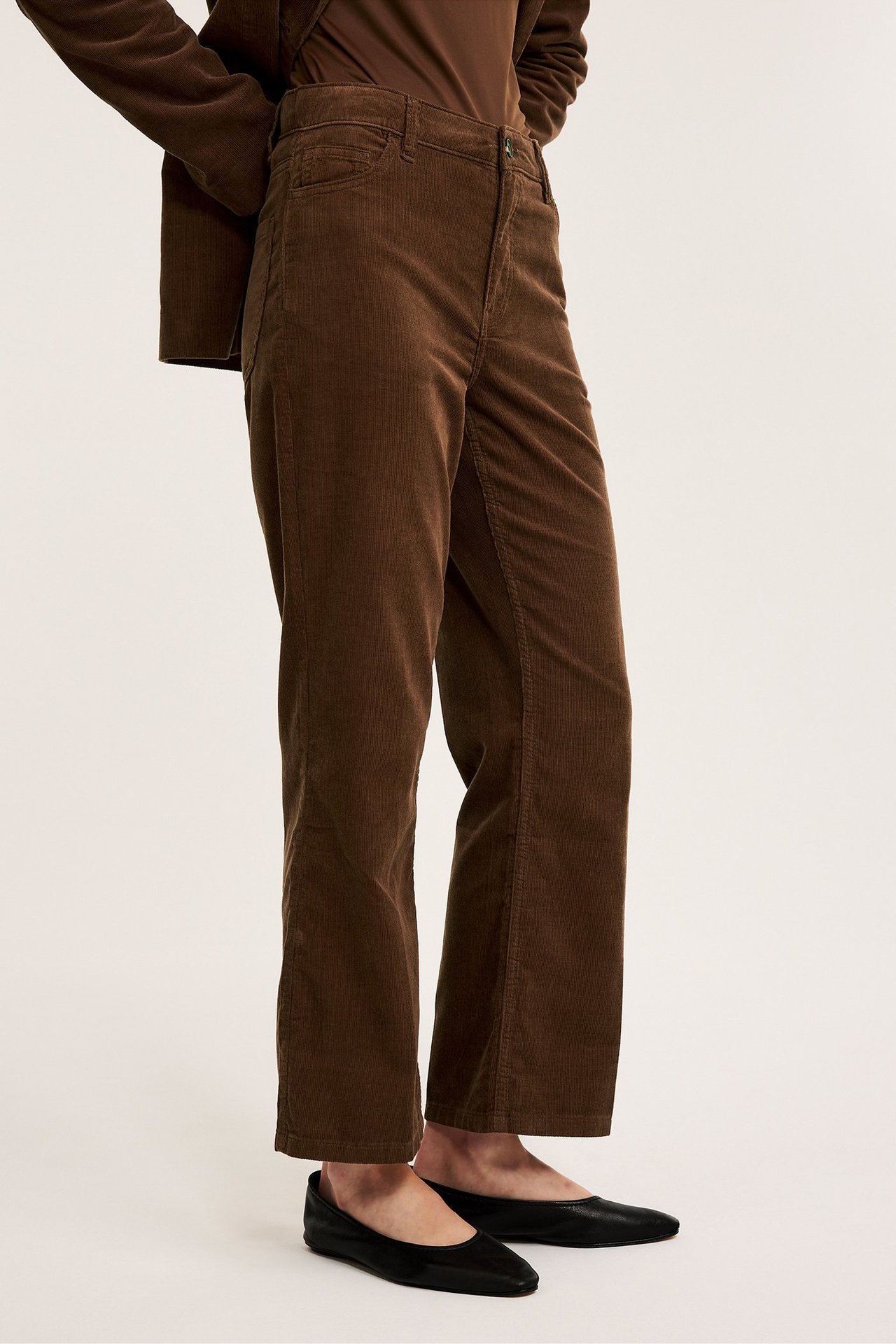 Edestä: Nainen ruskeissa vakosamettihousuissa, joissa kick flare -lahkeet, ruskea toppi, takki ja mustat ballerinat.