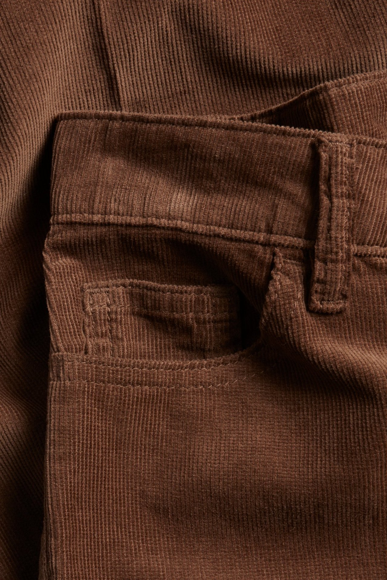 Zbliżenie brązowych sztruksowych spodni, pokazujące pas, szlufki i przednią kieszeń.