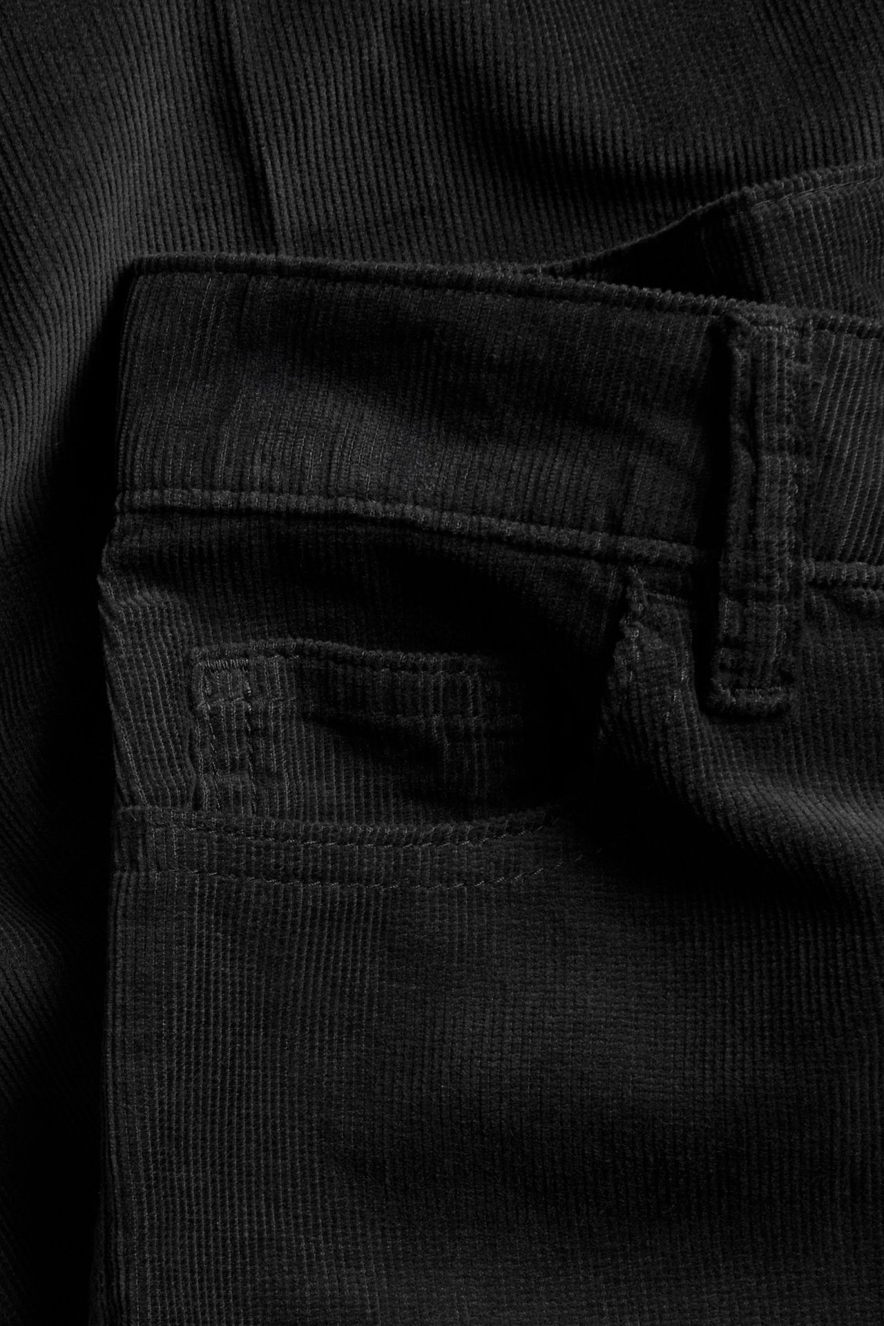 Zbliżenie czarnych sztruksowych spodni, pokazujące pas, szlufkę i małą kieszeń.