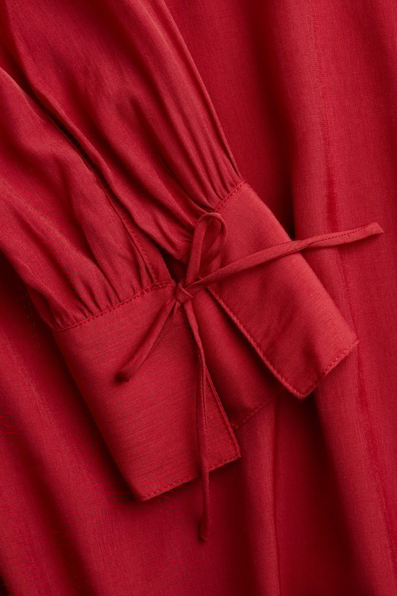 Zbliżenie na gładką czerwoną bluzkę z długim rękawem i wiązaniem przy mankiecie.
