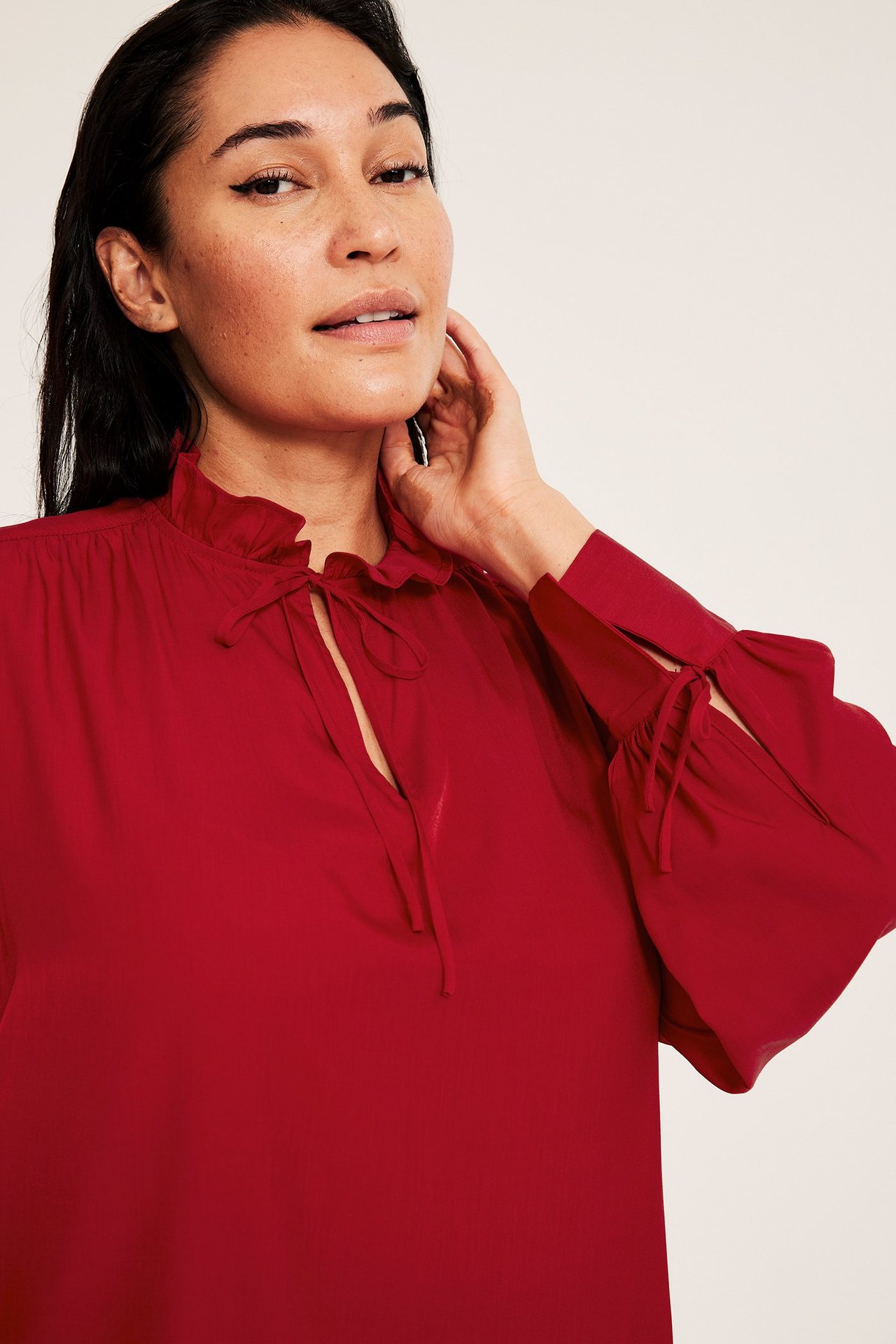 Zbliżenie kobiety w czerwonej bluzce z długim rękawem, falbanami przy kołnierzu i wiązaniem.