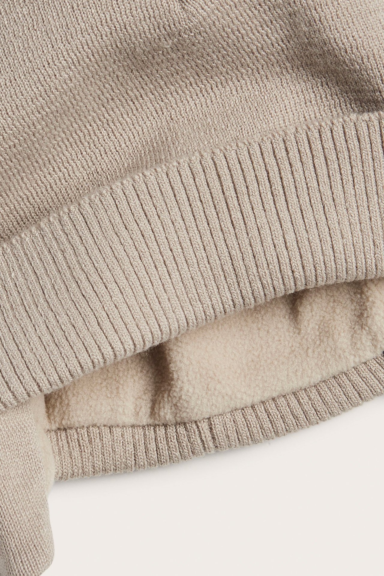 Närbild av en beige stickad mössa med ribbad kant och mjukt fleecefoder.