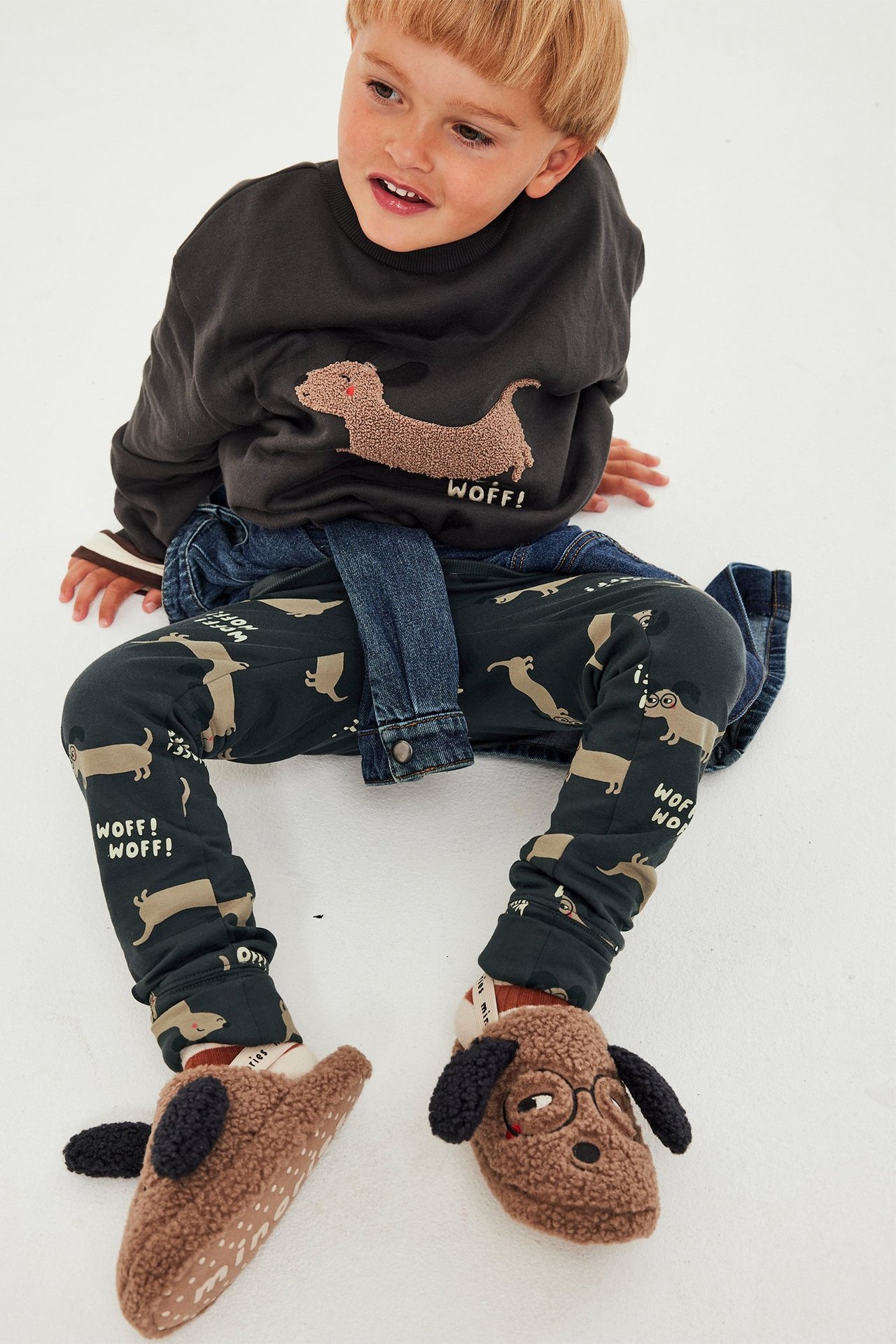 Frontvisning: barn i svarte mønstrede leggings med hundetrykk, mørkegrå genser, dongerijakke, hundetøfler.
