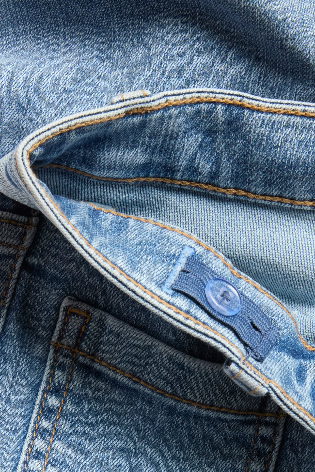 Zbliżenie na jasnoniebieskie dżinsy bootcut z regulowaną gumką i guzikiem w pasie, mid-waist.