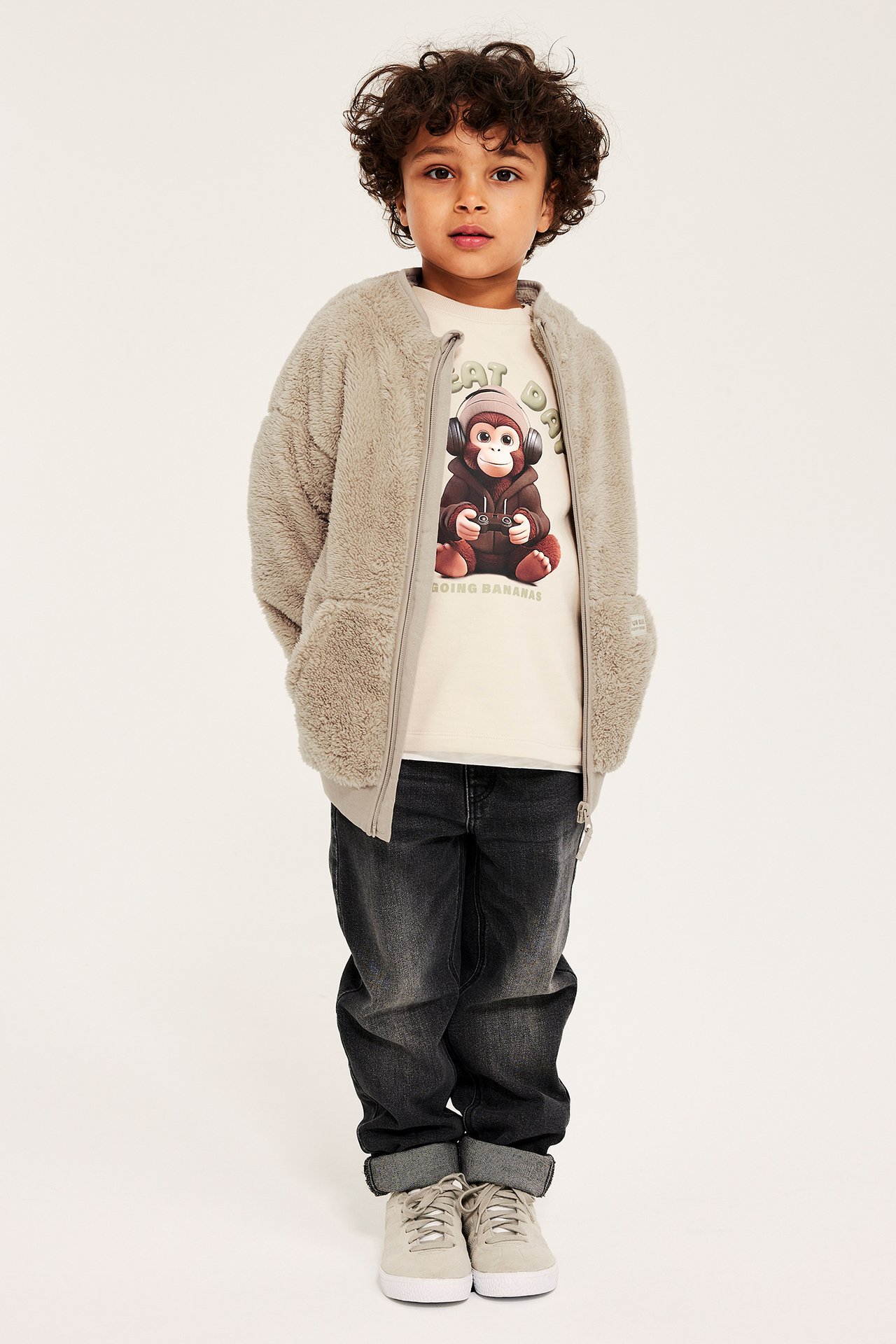 Lapsella beige piletakki, vaaleabeige apinaprinttipaita, tummanharmaat farkut, beiget lenkkarit.